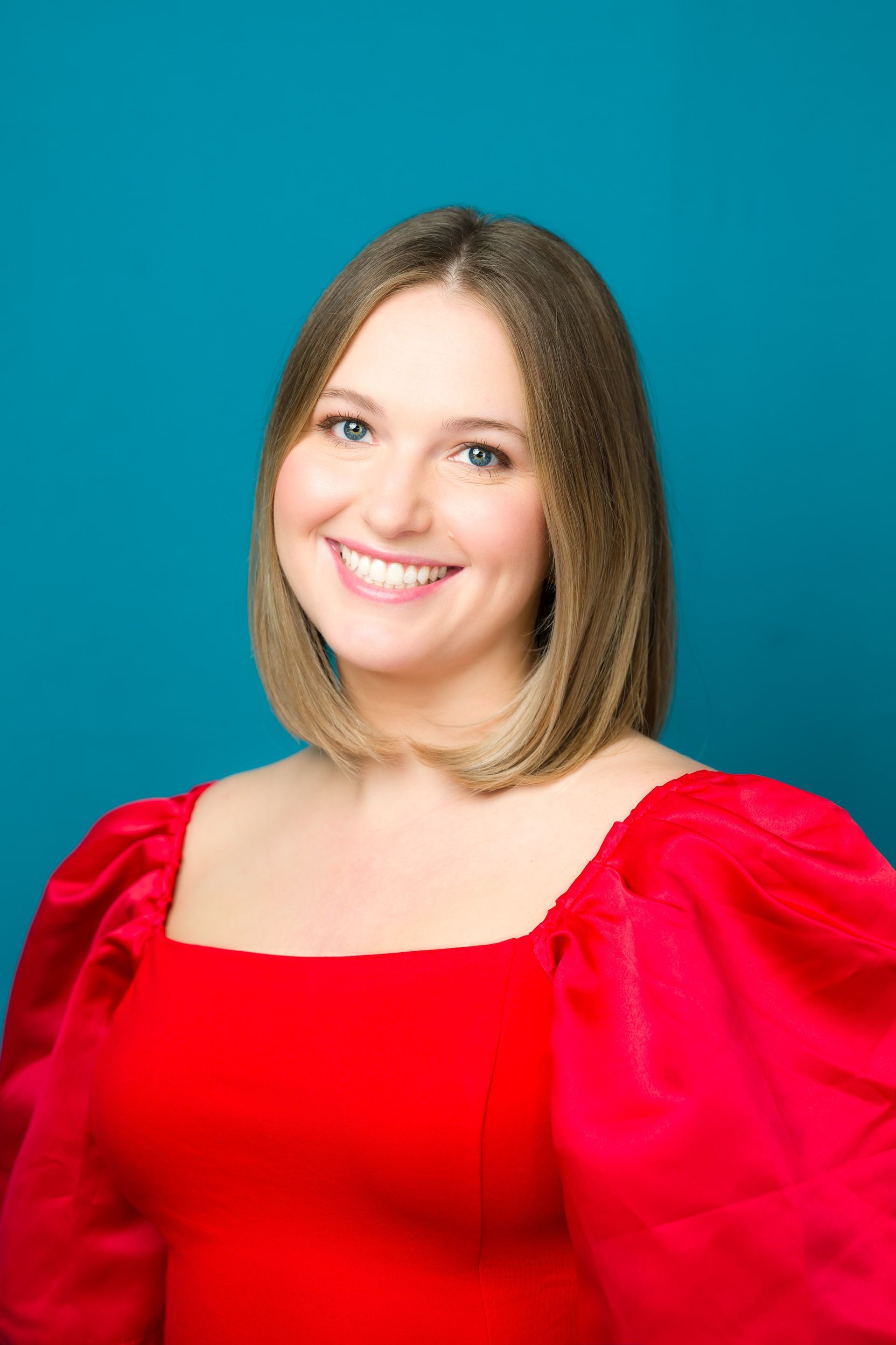 Woman with shoulder-length hair smiles in a red dress against a teal background.