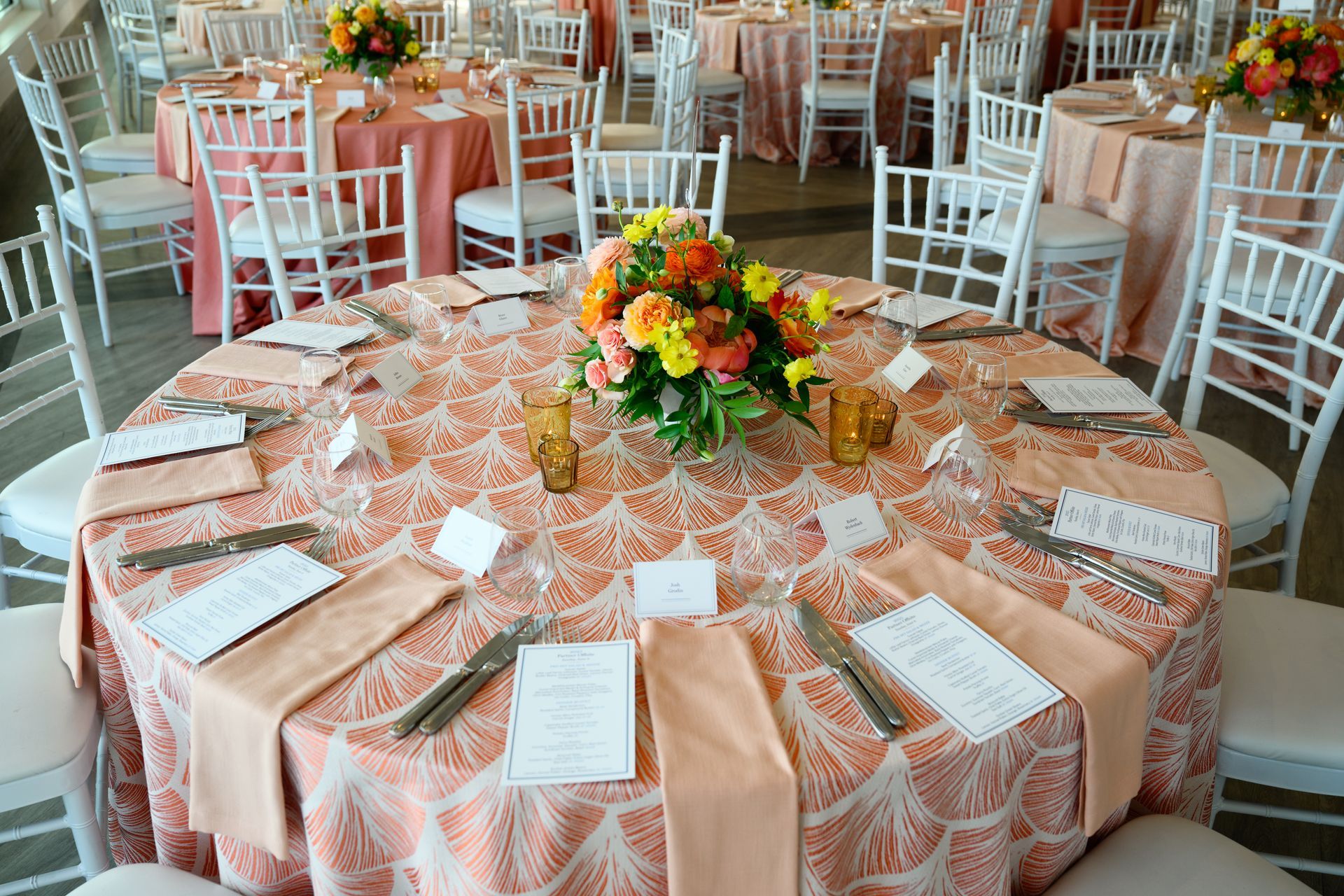 Round tables set for a wedding reception with peach linens, white chairs, and floral centerpieces.