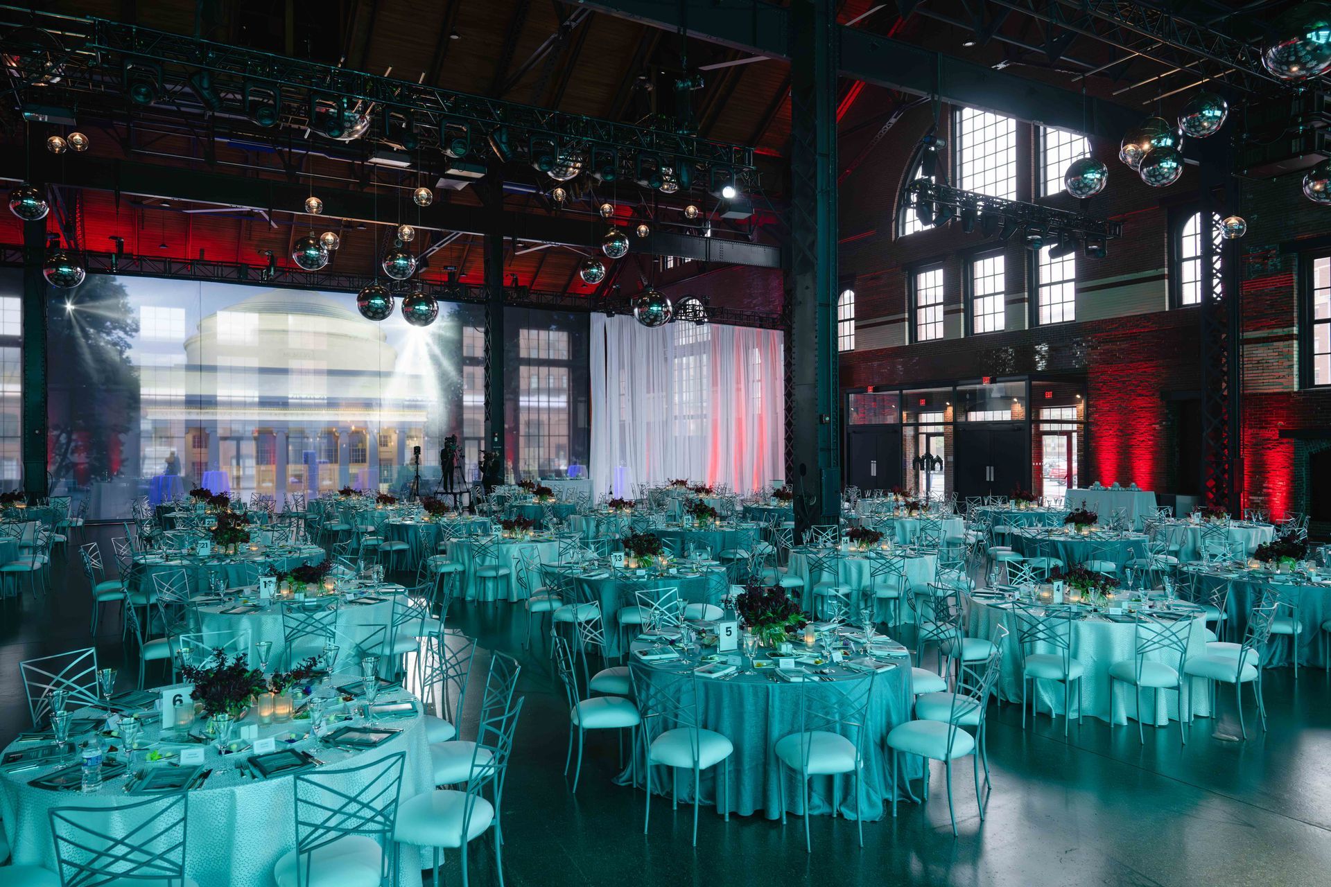 Ballroom with teal tables, white chairs, and disco balls; red uplighting.