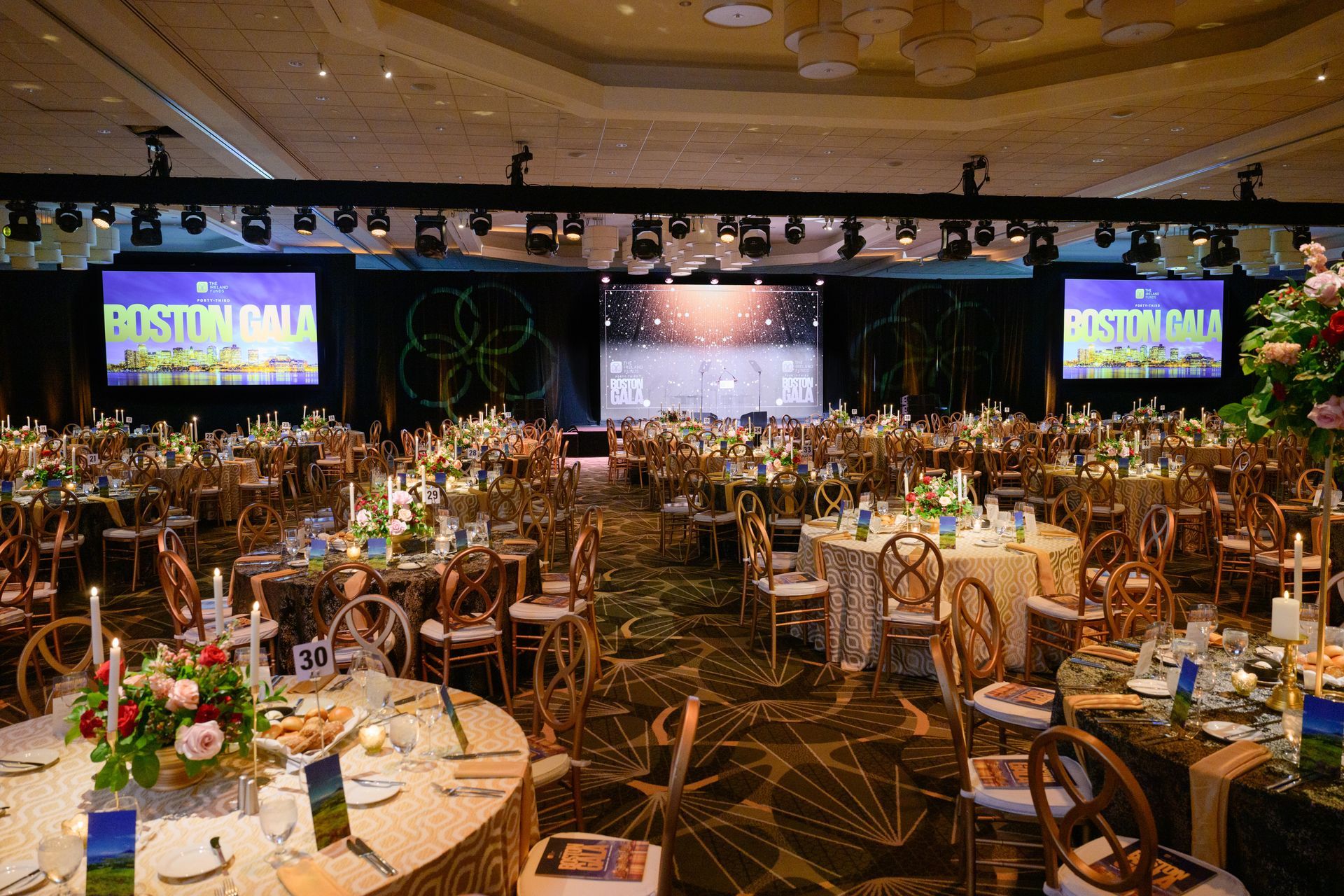 Formal banquet hall set for an event; tables, chairs, decorations, and screens with