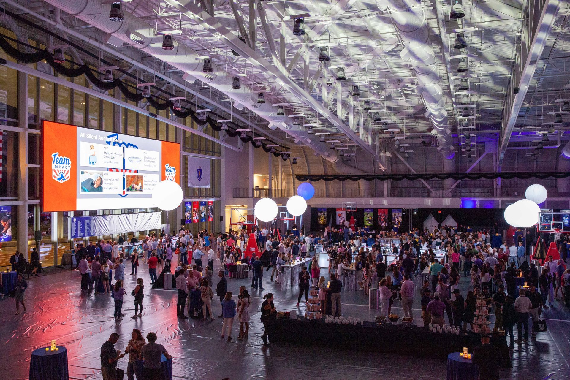 Large event hall with crowd, large screen displaying graphics, decorative lights, and dark ceiling.