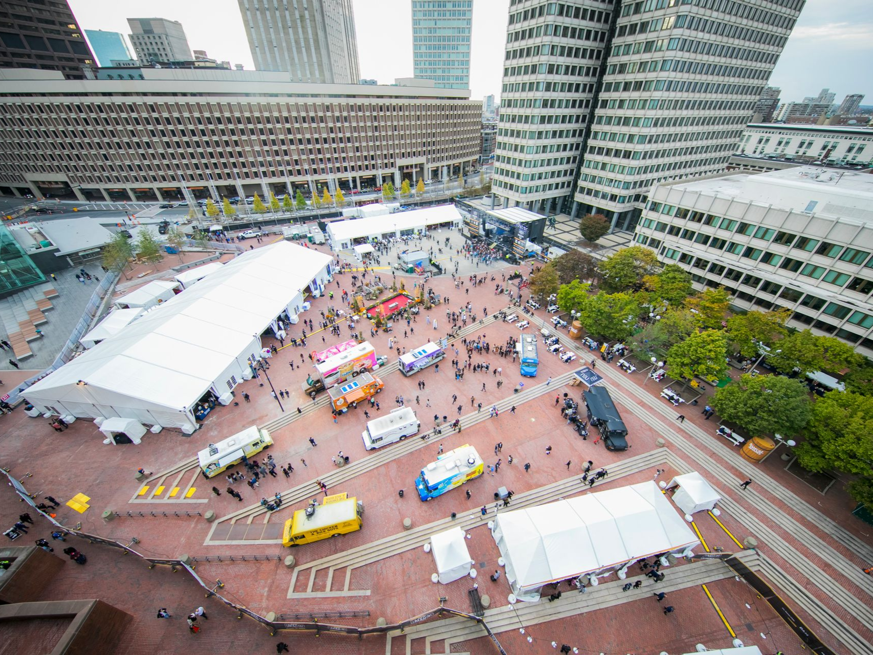 Aerial view of a food truck festival in a city square, with people, tents, and buildings.