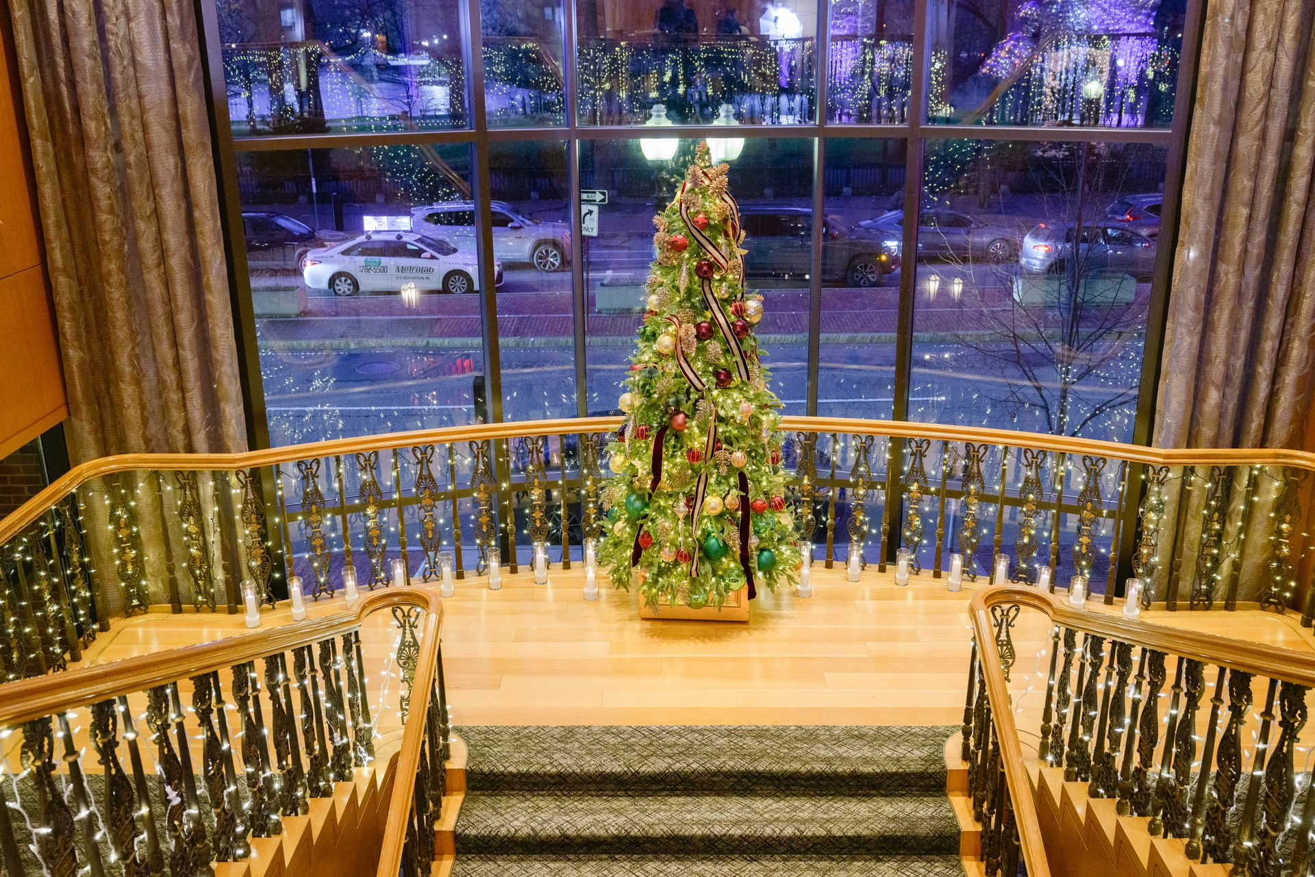 Christmas tree inside a building, viewed through a large window overlooking a street at night.