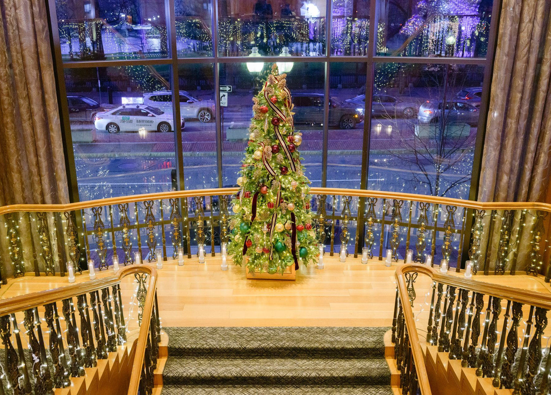 Christmas tree inside building, looking out a large window at a city street at night.
