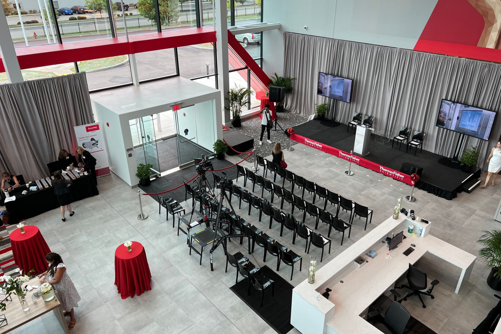 An event setup in a modern building with a stage, rows of chairs, and red and white accents.