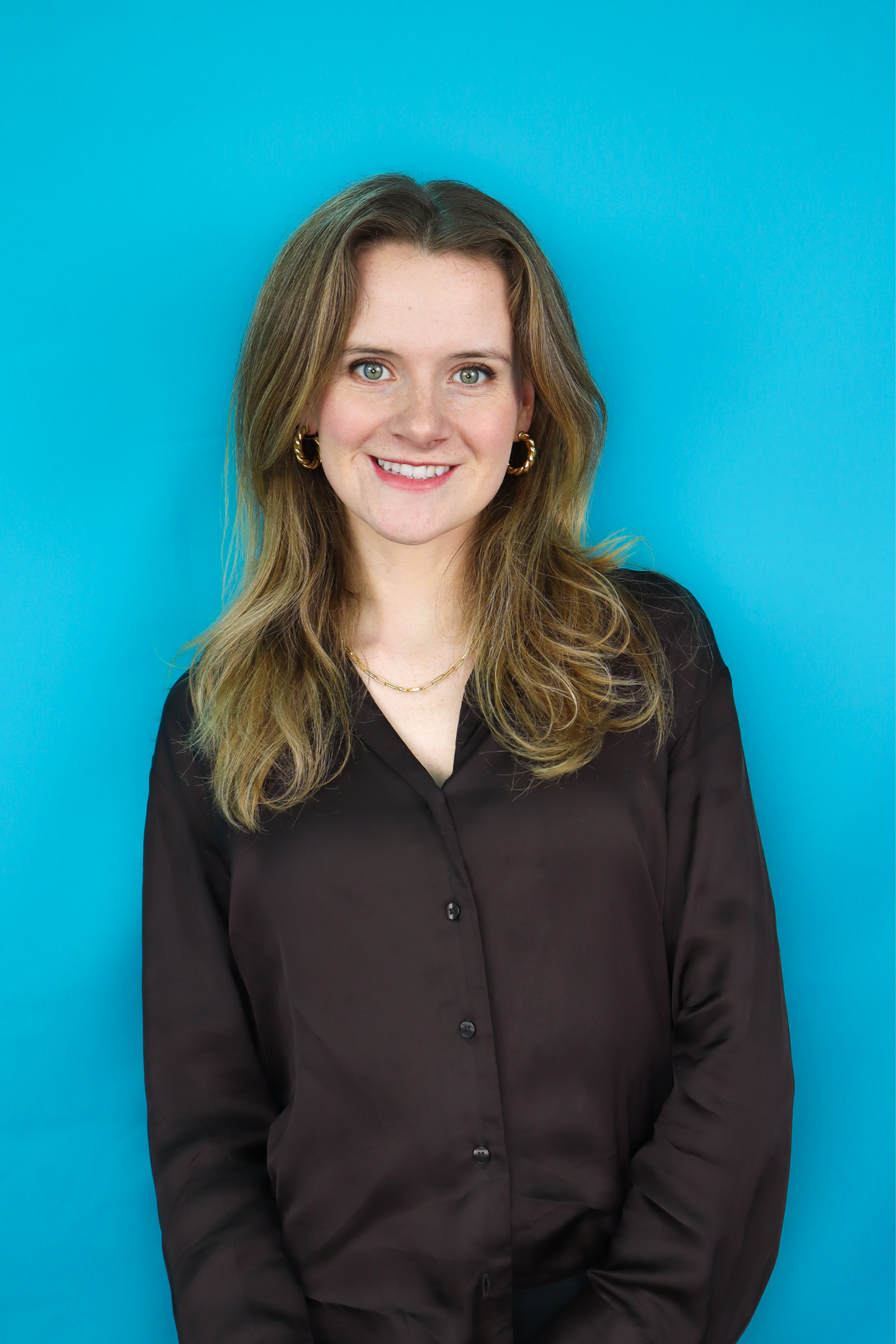 A woman in a purple dress is smiling in front of a blue background.