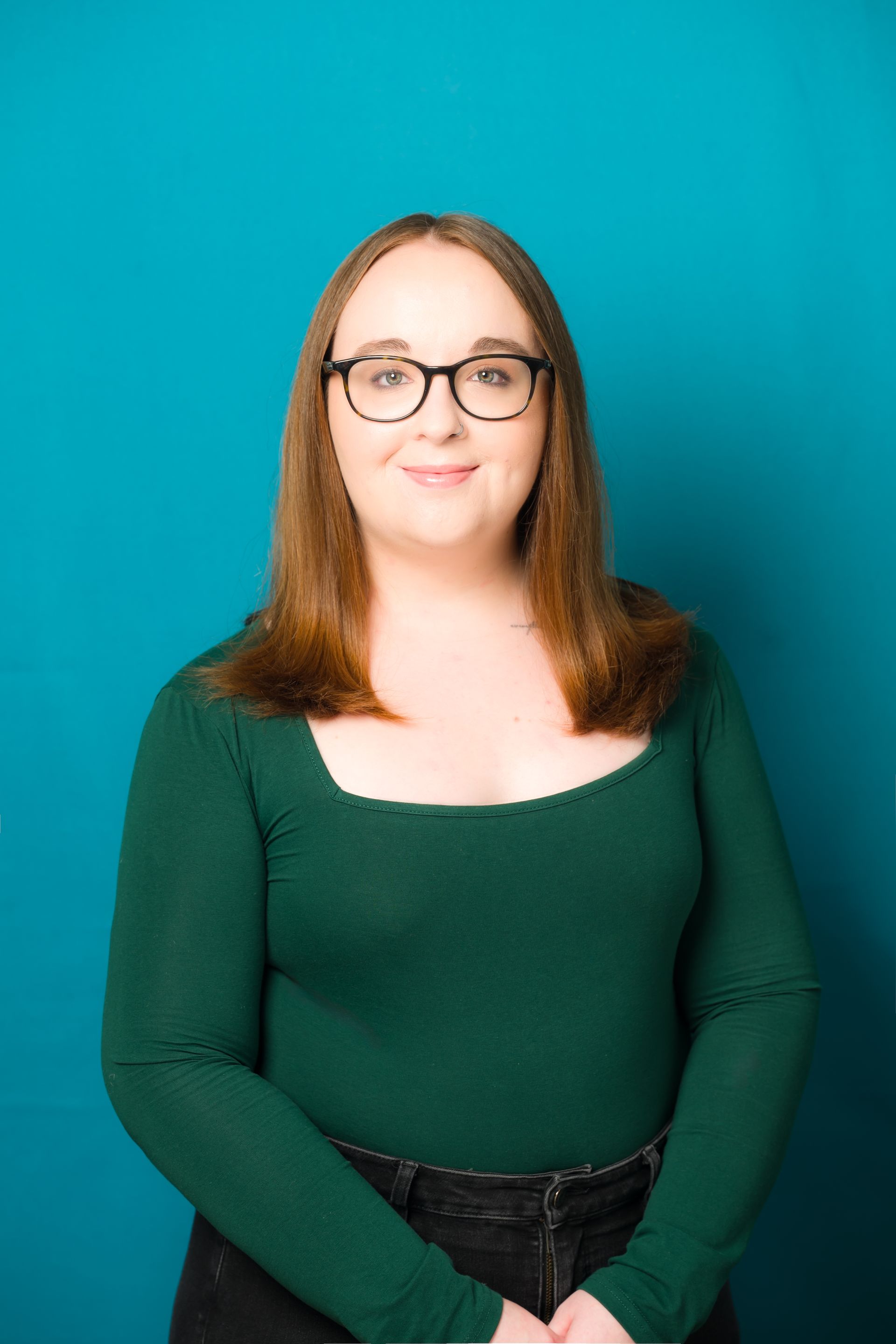 A woman wearing glasses and a green shirt is standing in front of a blue background.