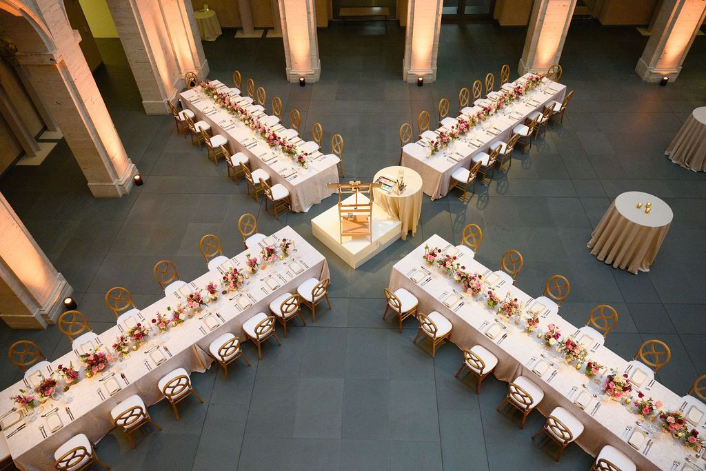 Formal event setup in a large hall: long tables radiating from a central platform, gold chairs, white tablecloths.