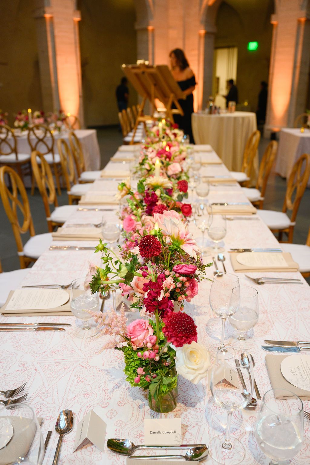 Long table set for an event with floral centerpiece, white tablecloth, and elegant chairs.