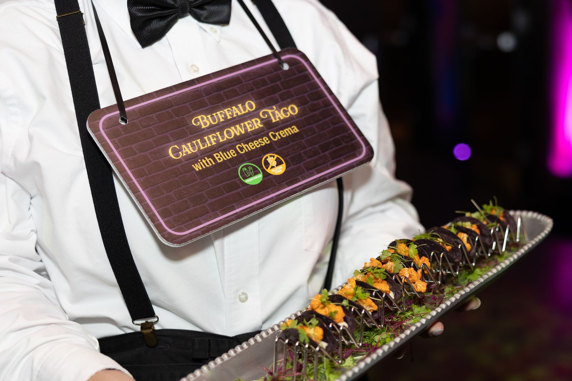 Server presenting a tray of sushi rolls with garnish and a maroon sign on the chest