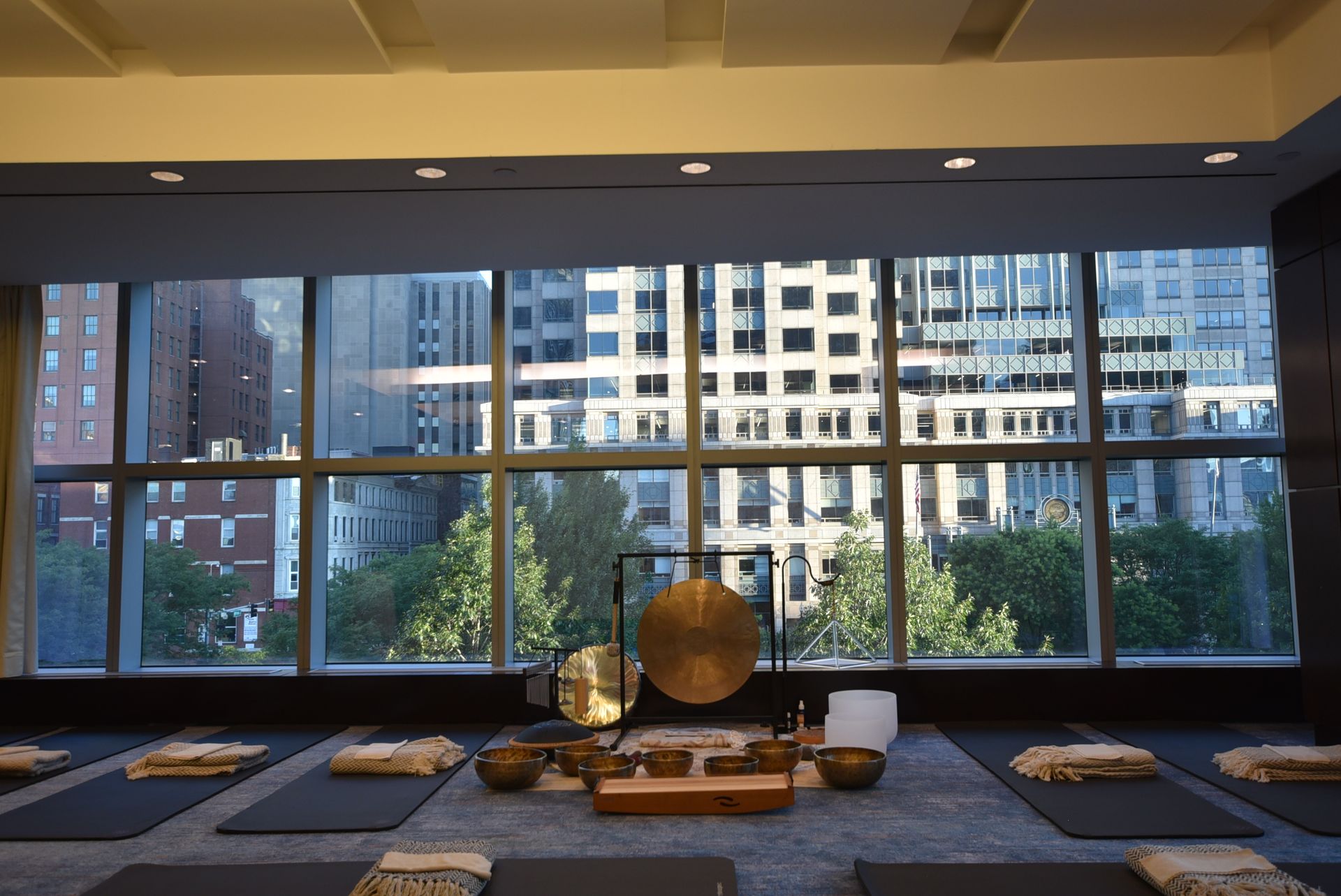 Yoga studio with mats, instruments, and city view through large windows.
