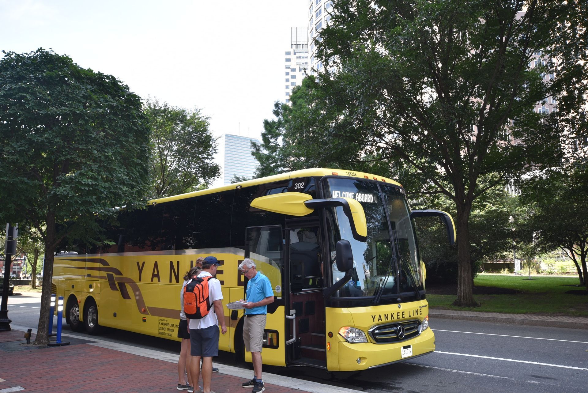Yellow charter bus parked next to a sidewalk with people standing nearby.