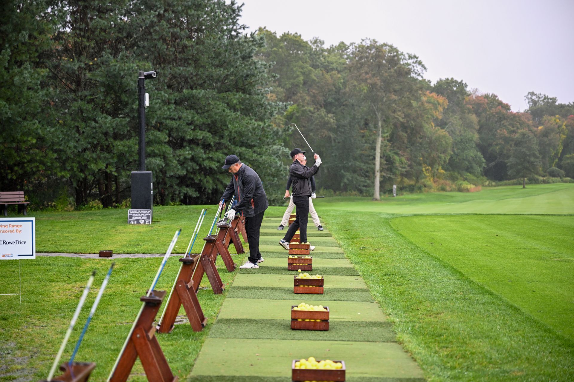 Two people practicing golf swings at a driving range on a green, grassy course.