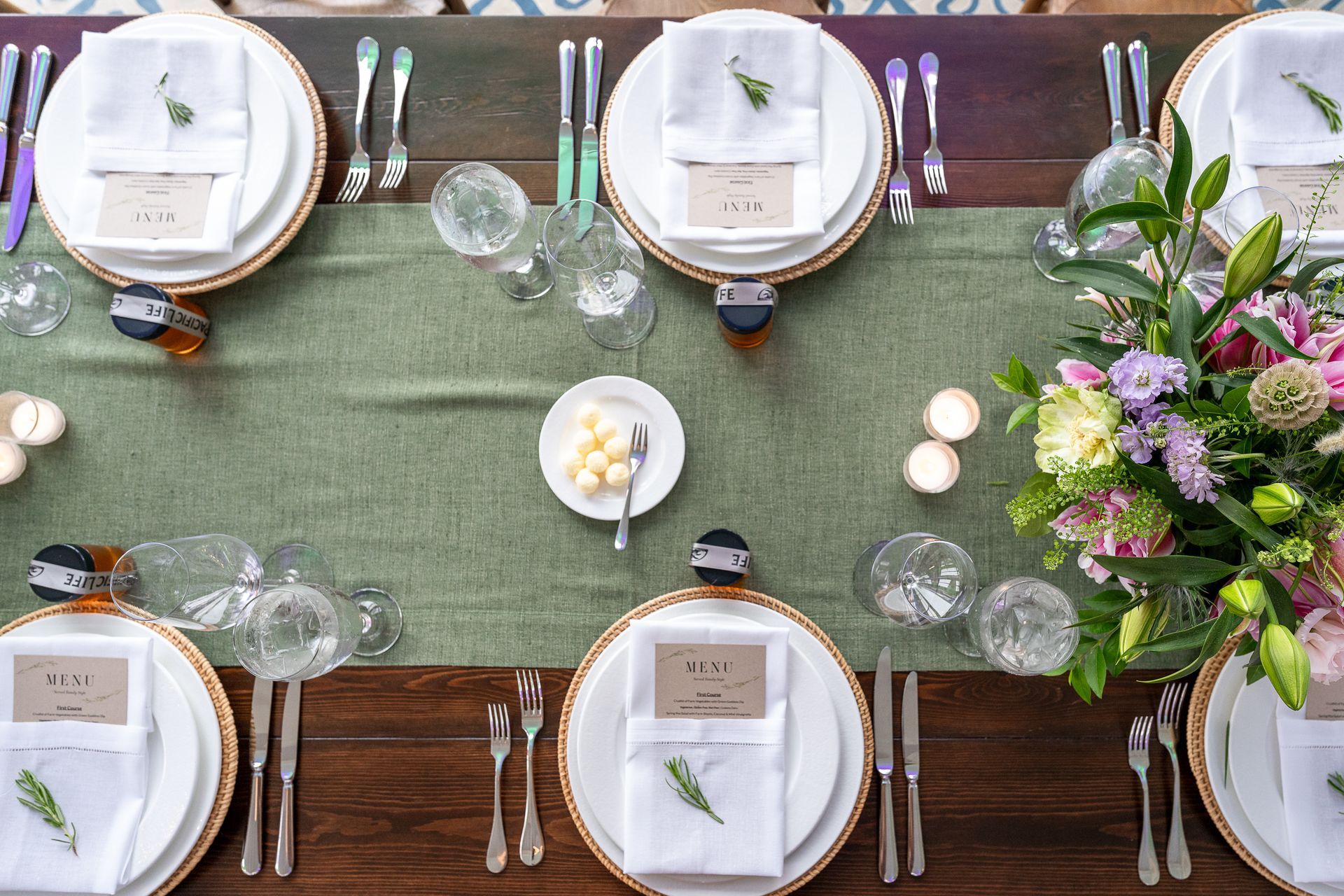 A long wooden table with plates , silverware , and flowers on it.