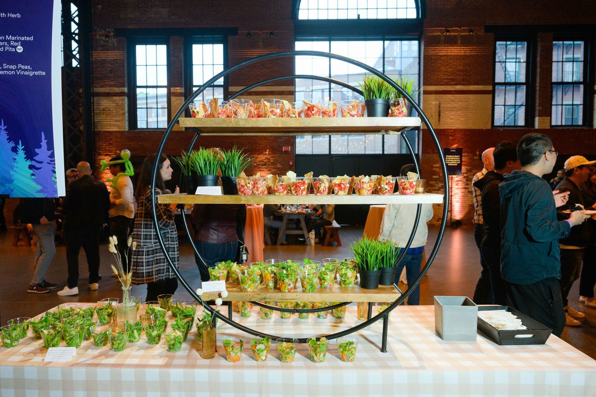 Food display on a tiered circular shelf, with attendees in a brick-walled event space.
