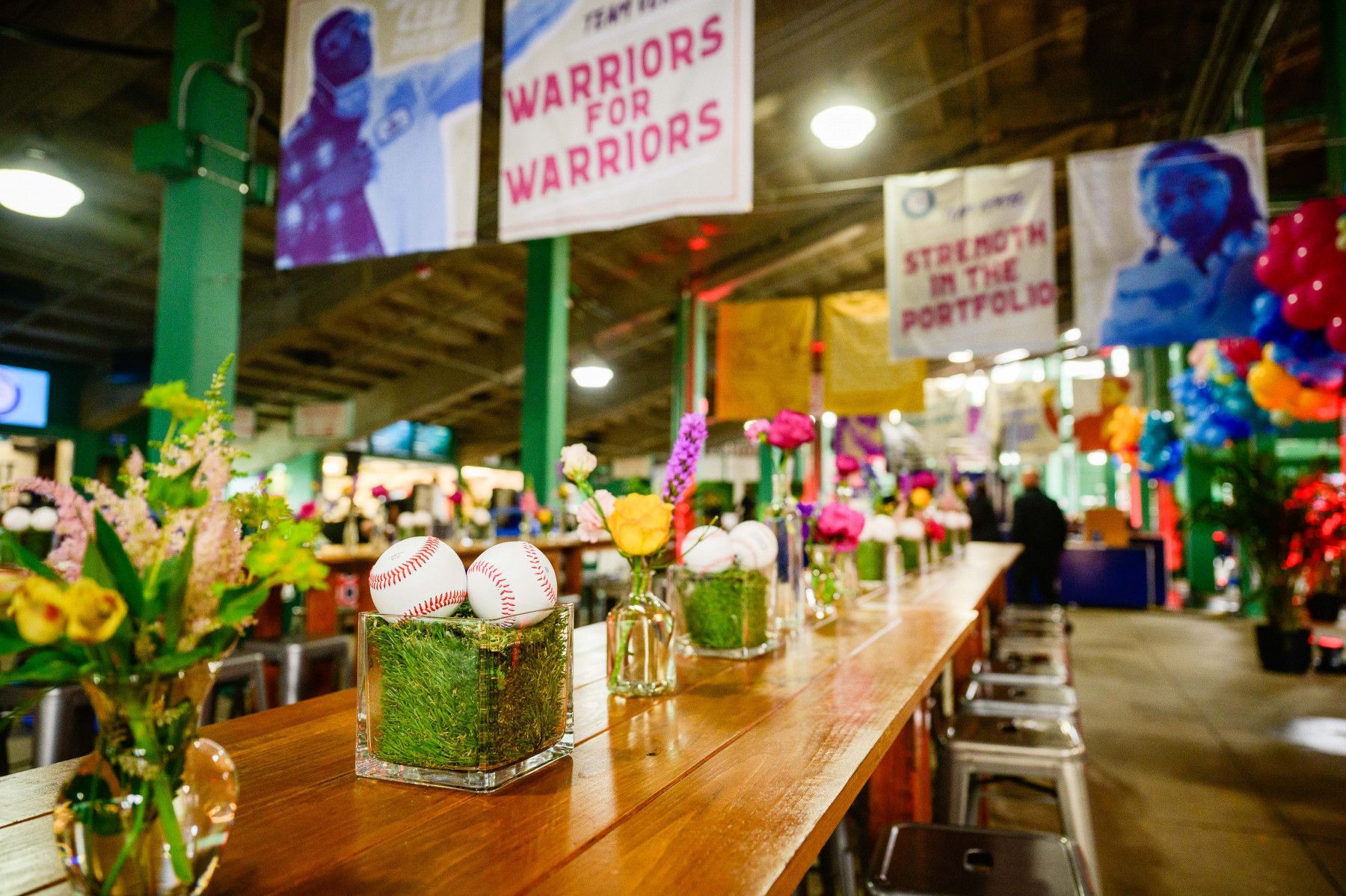 A long wooden table with flowers and baseballs on it.