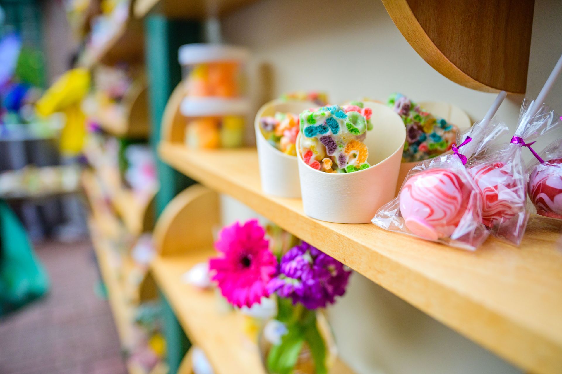 Candy and treats on a wooden shelf, including colorful popcorn, wrapped candy apples, and flowers.