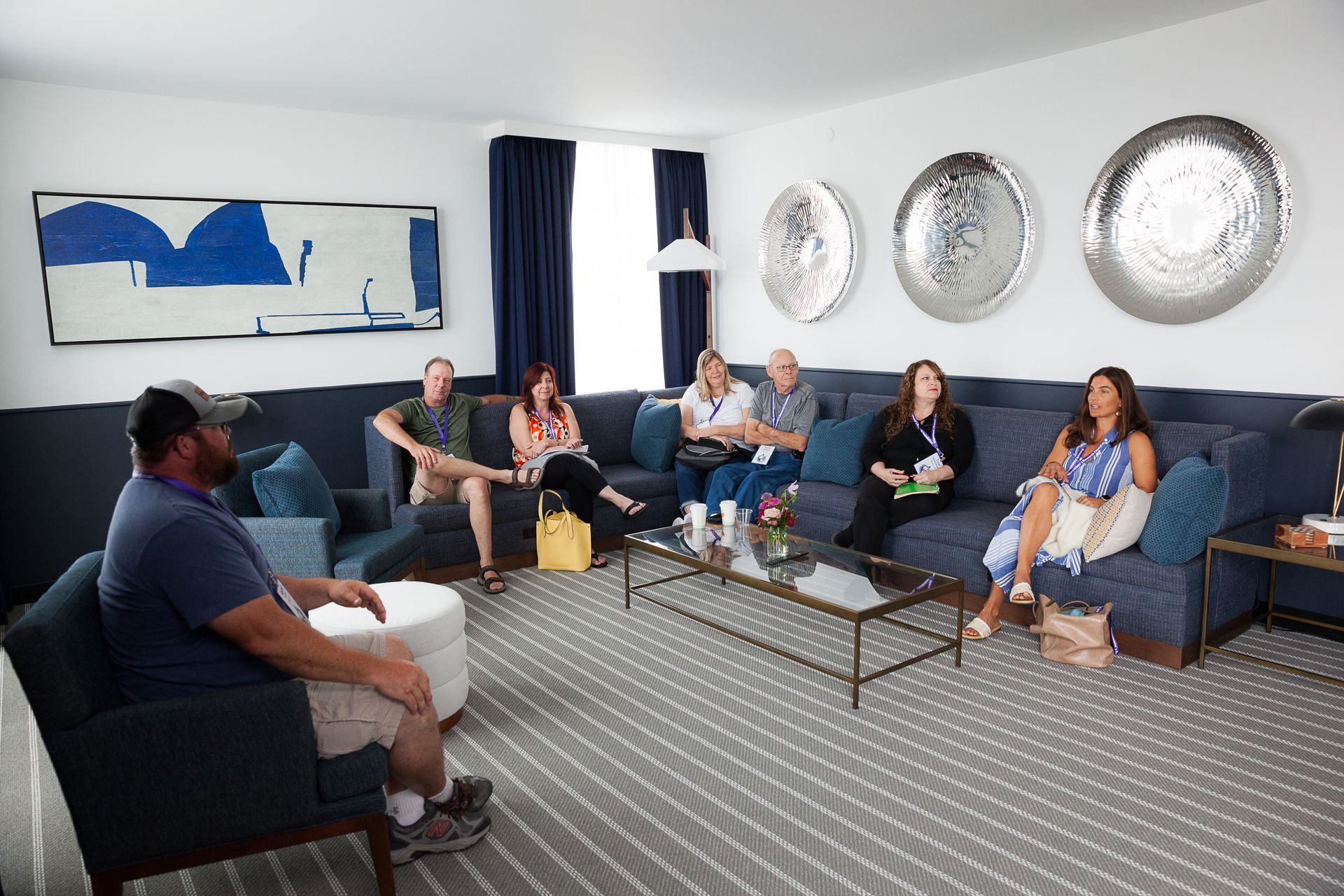 People in a blue-themed living room, sitting on a sectional sofa and chairs, engaged in conversation.
