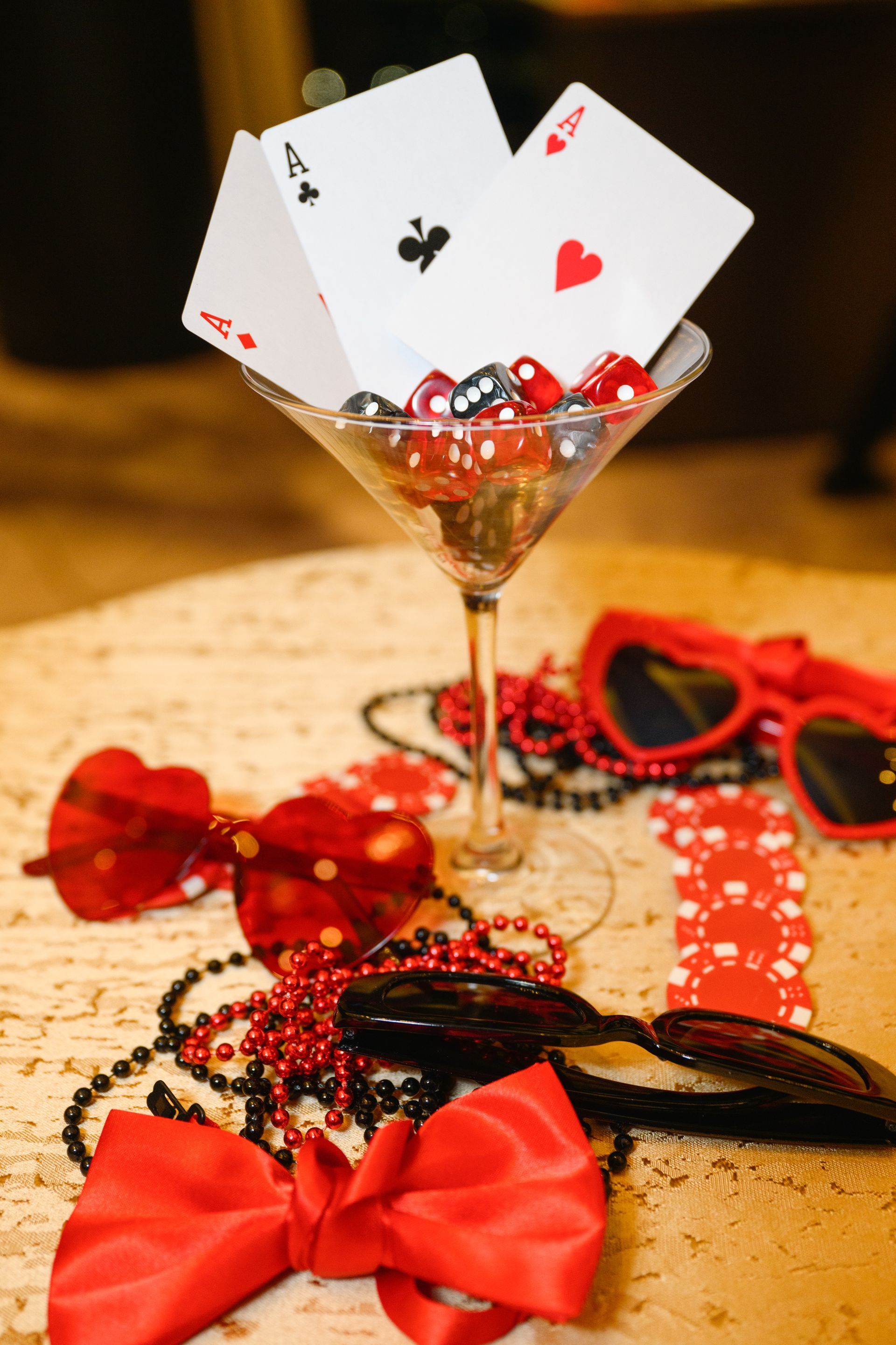 Cocktail glass with cards & dice, surrounded by red sunglasses, beads, bow tie, and poker chips.