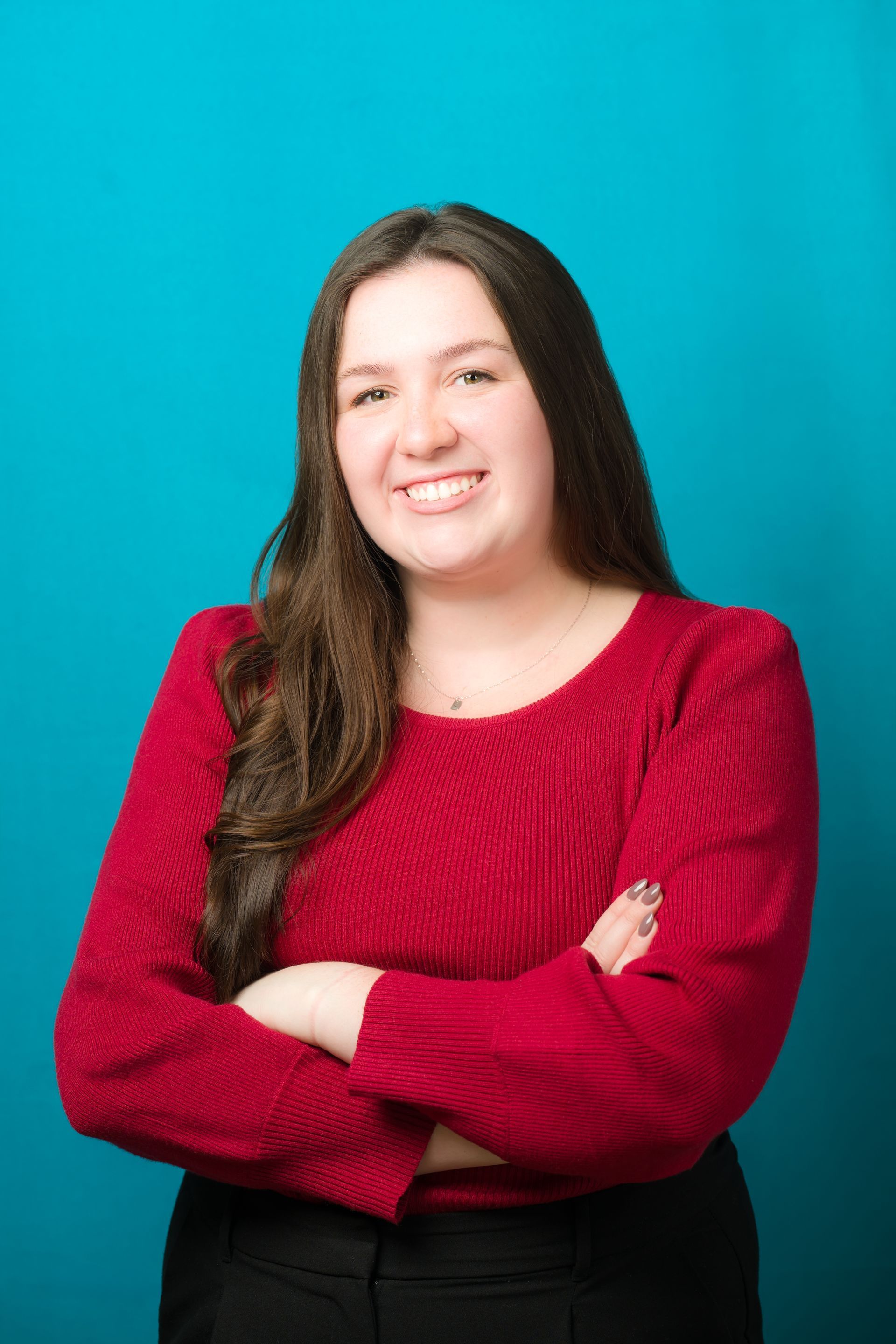 Woman with long brown hair, red sweater, arms crossed, smiling.