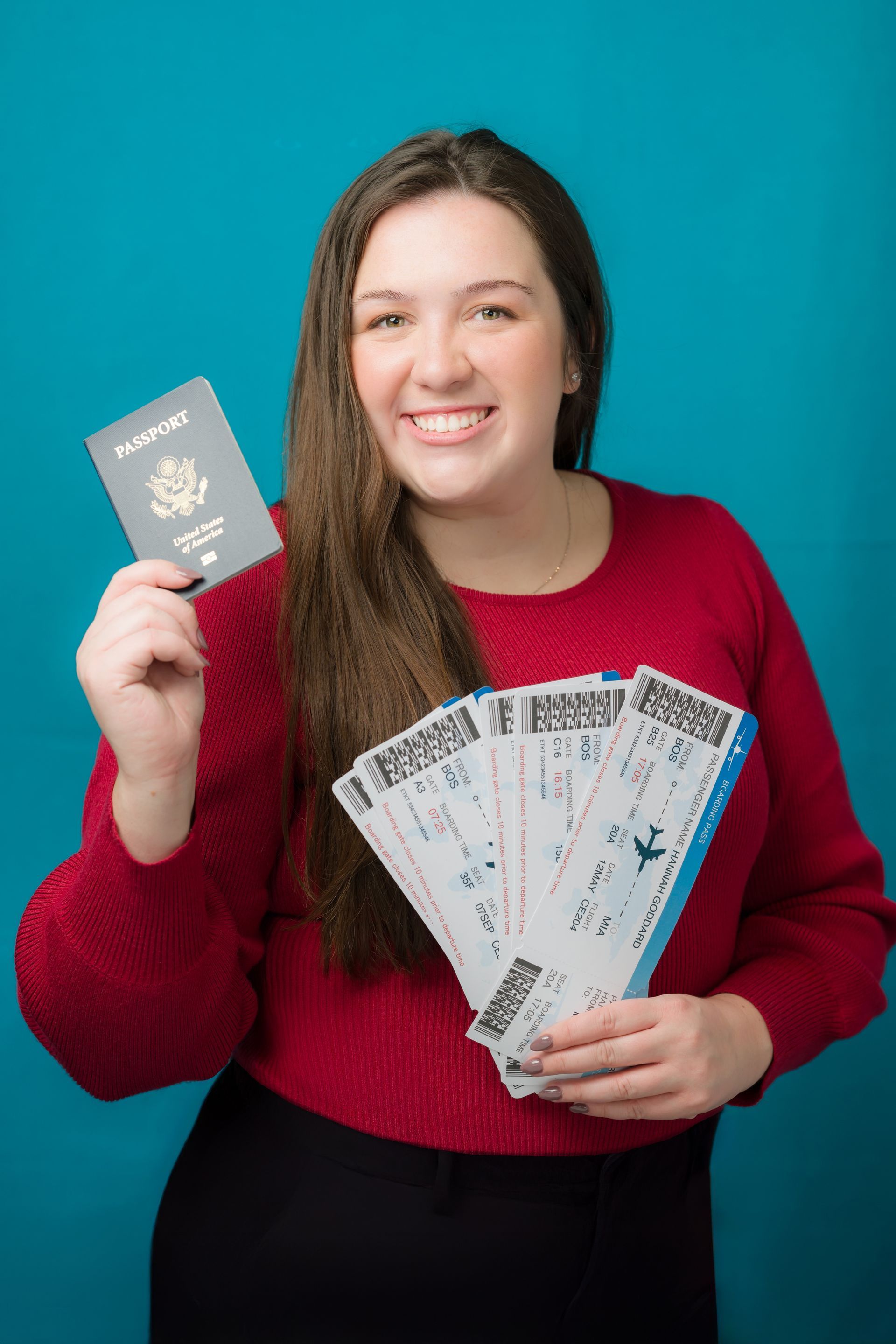 Woman holding a passport and multiple plane tickets, smiling, red sweater, blue background.