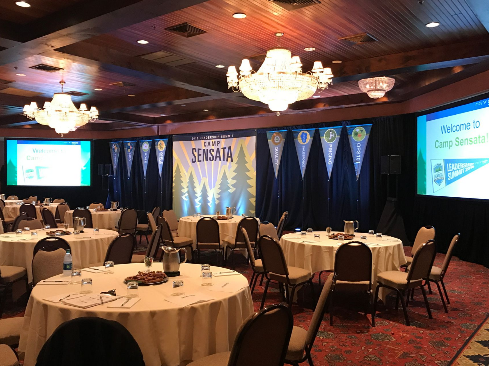 A banquet hall set for a conference with round tables, chairs, screens, and banners.