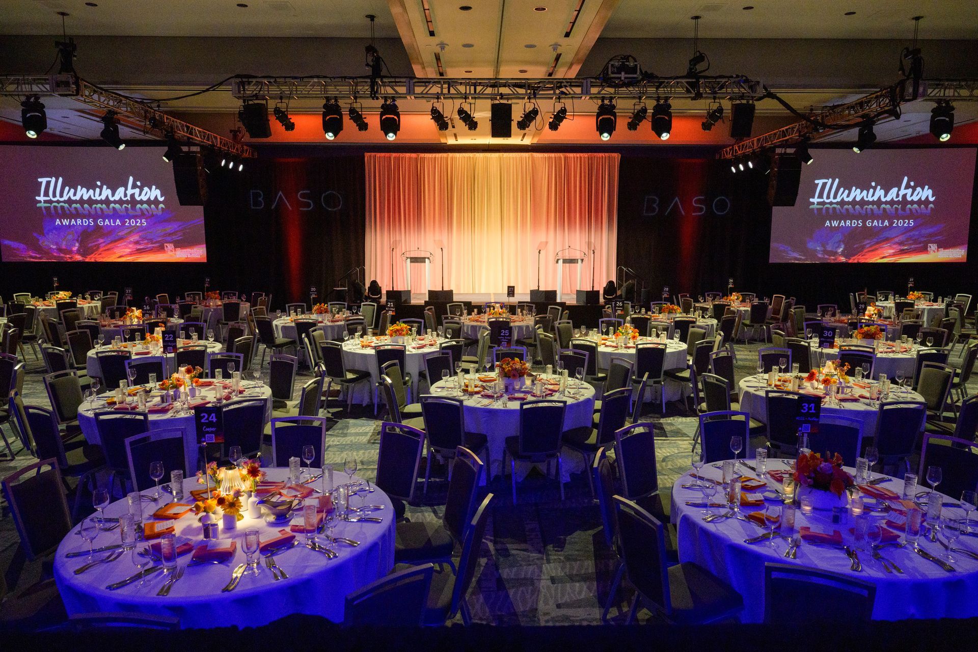 A large banquet hall set for a conference with round tables and a stage with a backdrop.