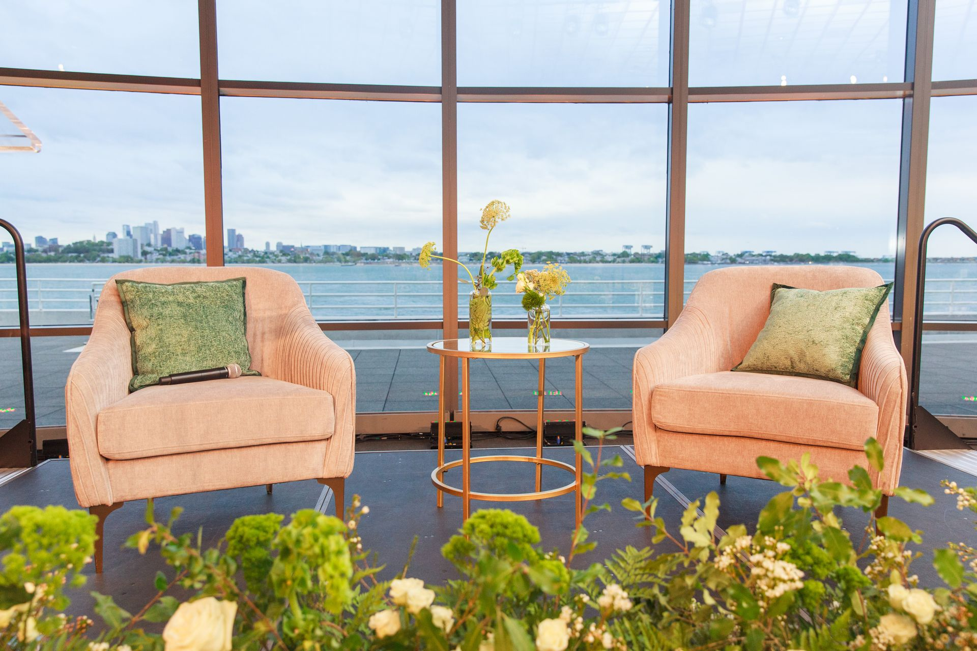 Two peach armchairs, small gold table, floral arrangement, and water view.