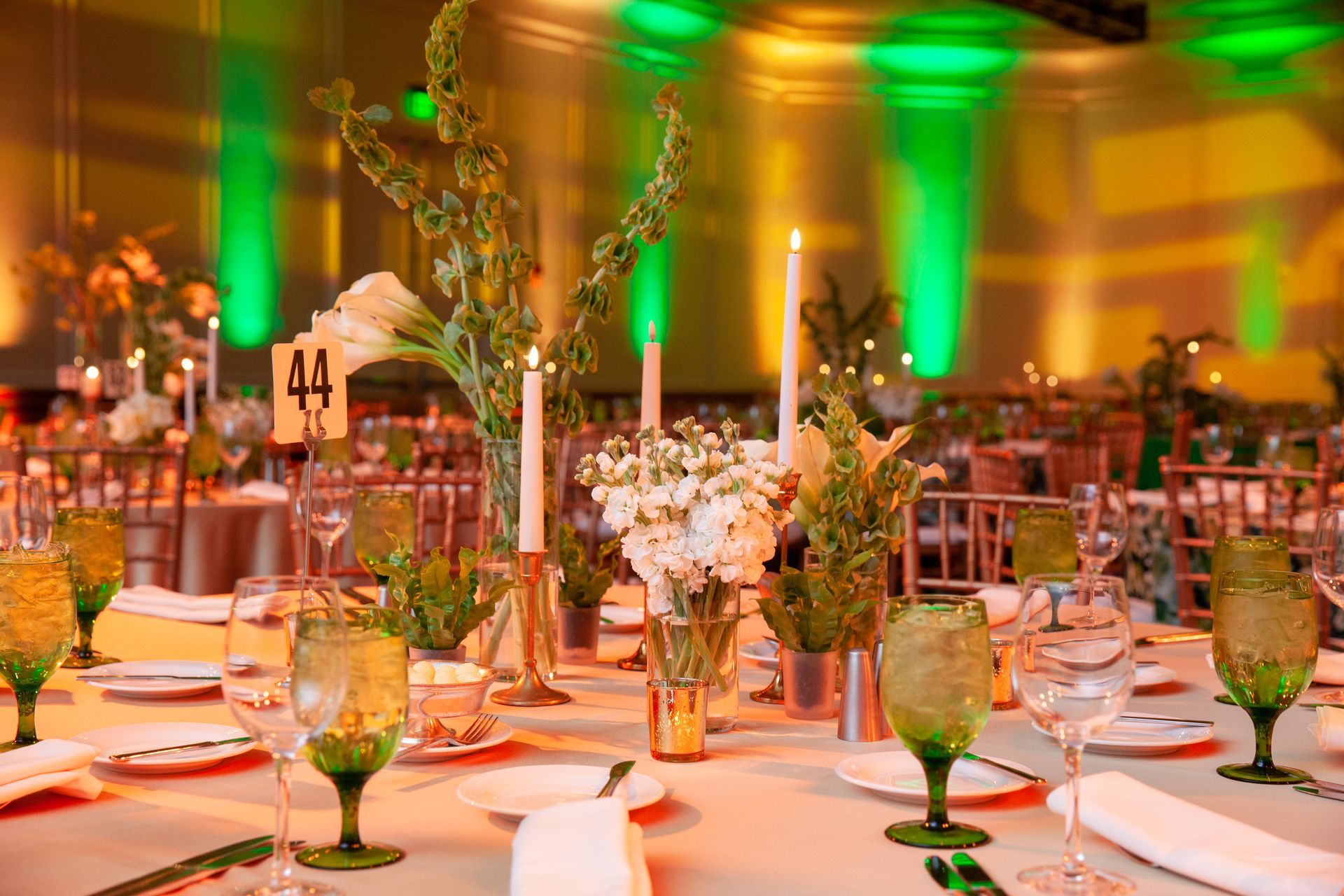 Elegant table setting with green-tinted glassware and floral centerpieces under green stage lighting.