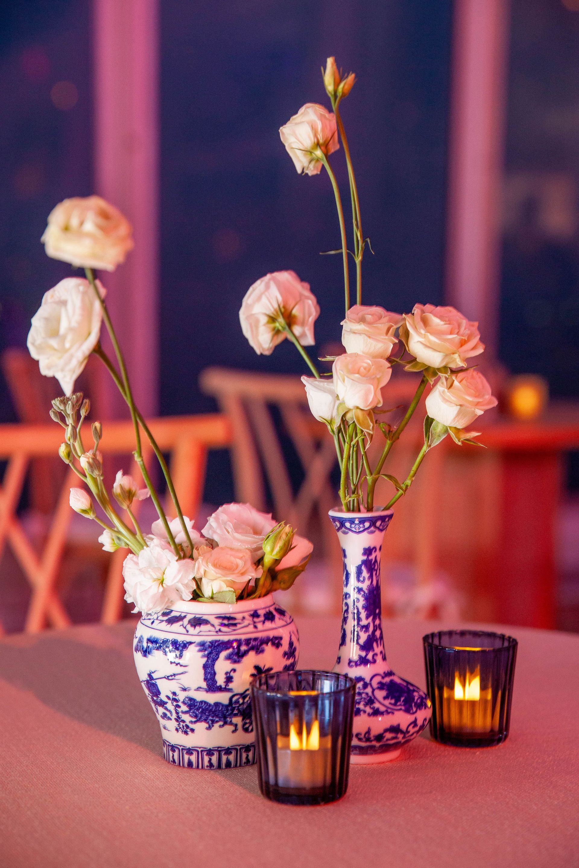 White roses in blue and white vases with lit candles on a table.