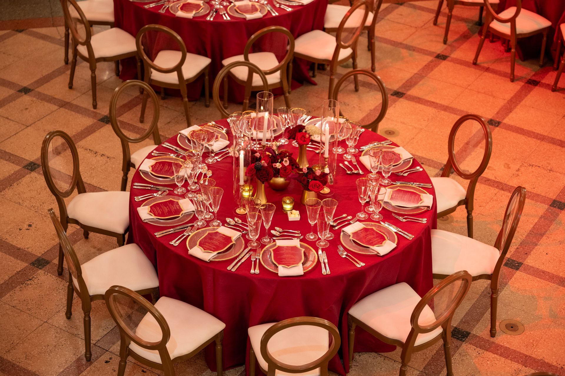 Round tables set with red tablecloths, white chairs, and elegant place settings.
