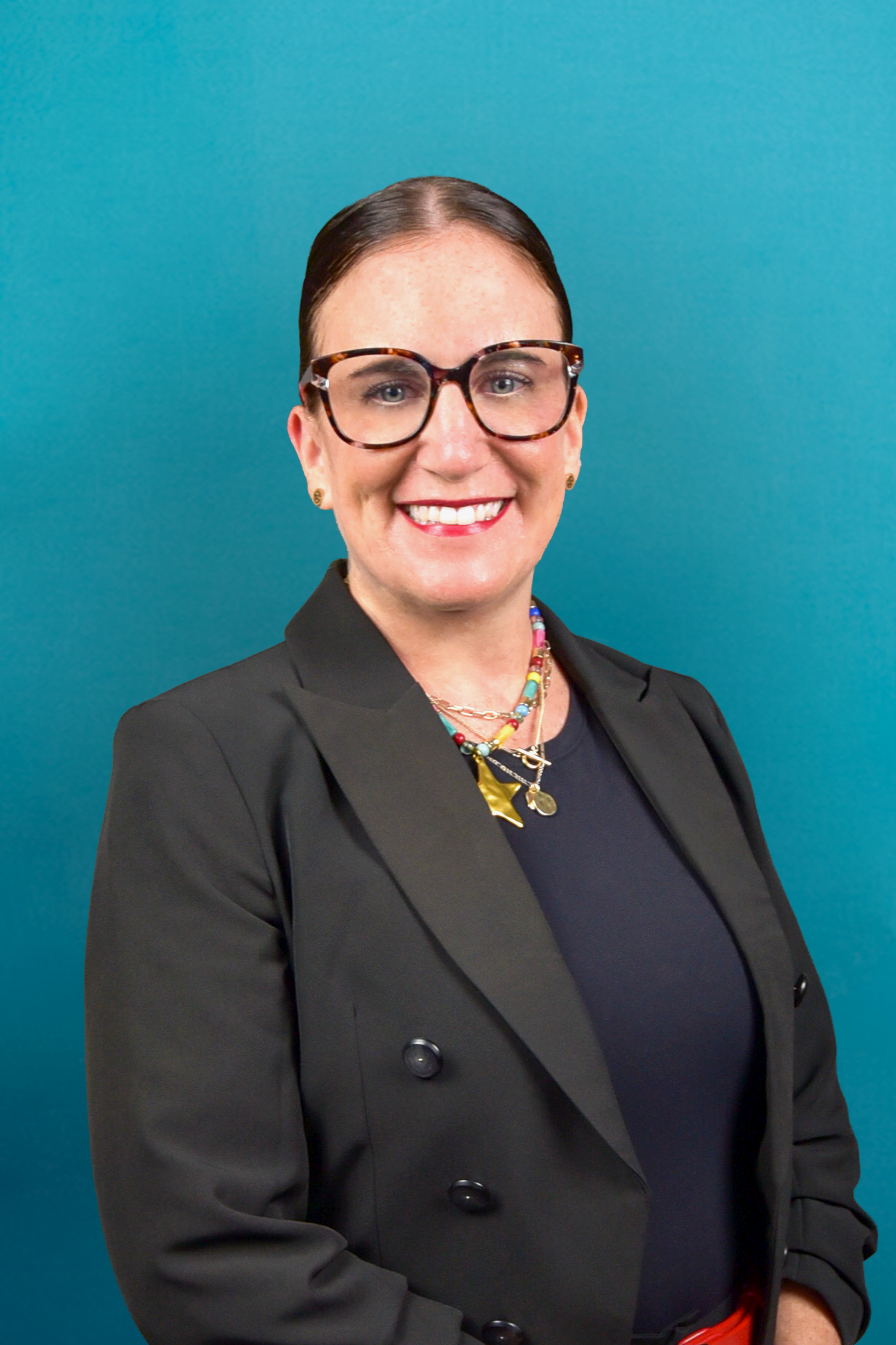 Smiling person in glasses and black blazer against a teal background