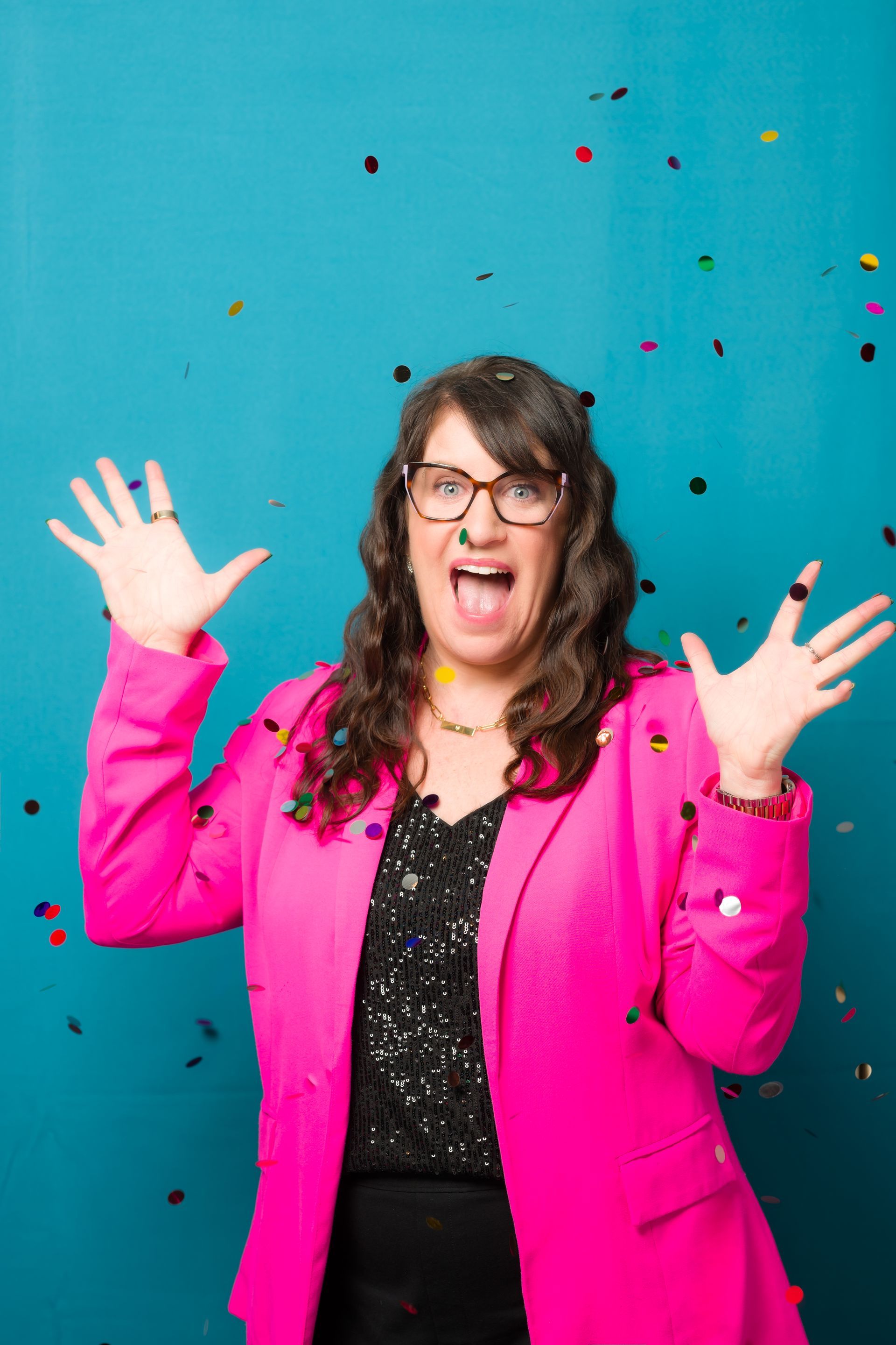 Woman in pink blazer, arms raised, mouth open, confetti falling against a teal background.