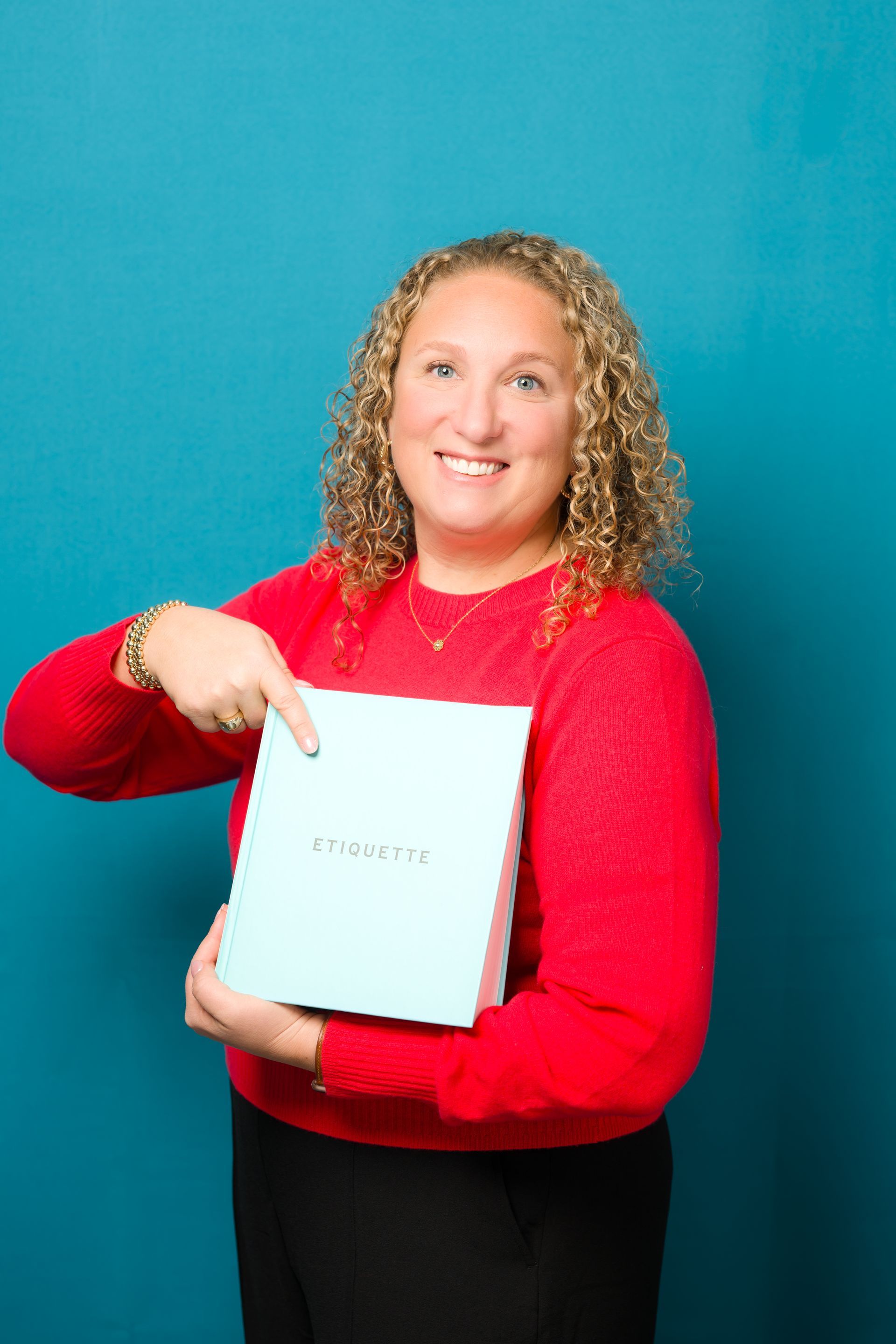 Woman in red sweater, pointing at a light blue box with text against a teal background.