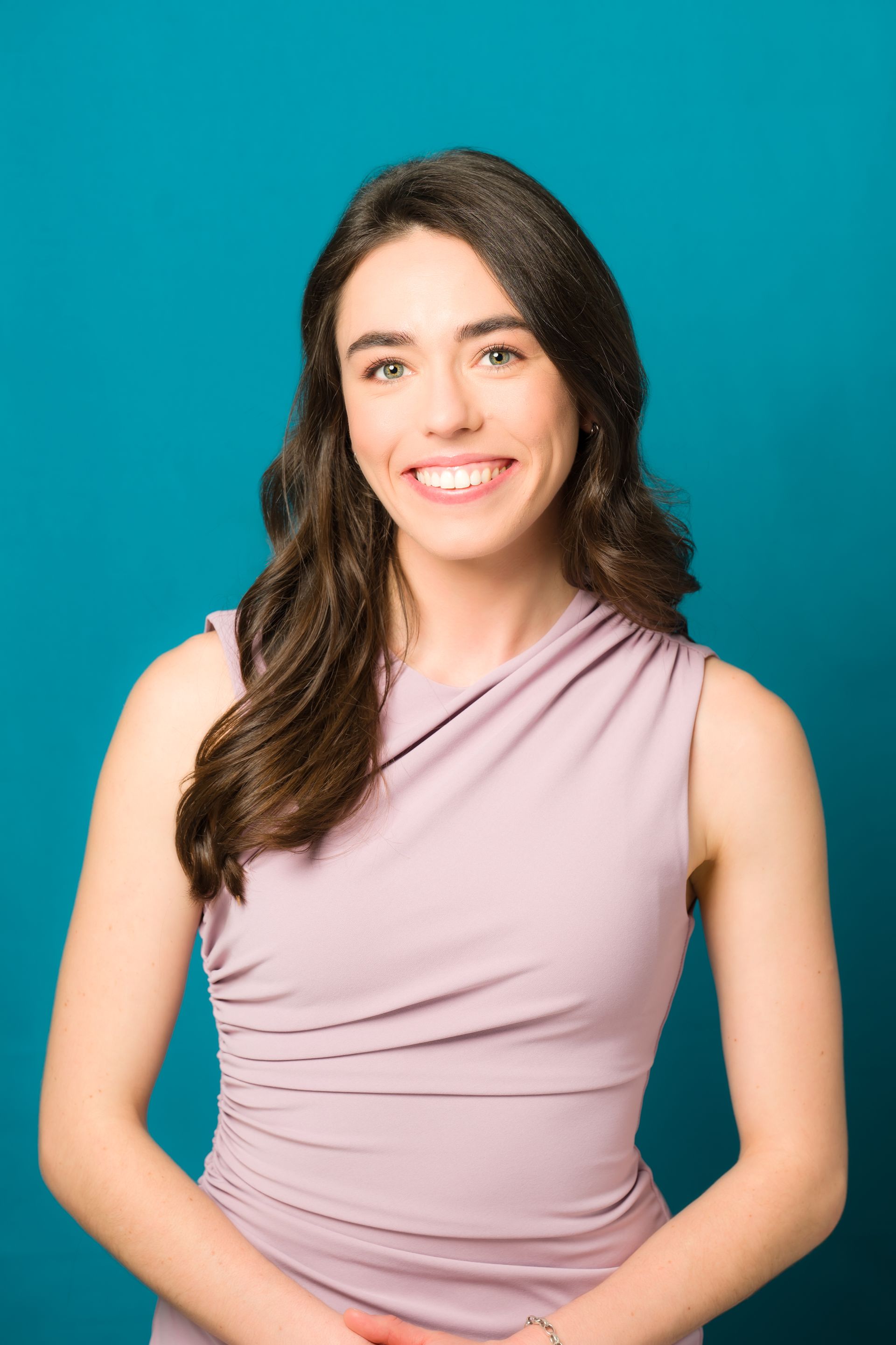 A woman in a purple dress is smiling in front of a blue background.