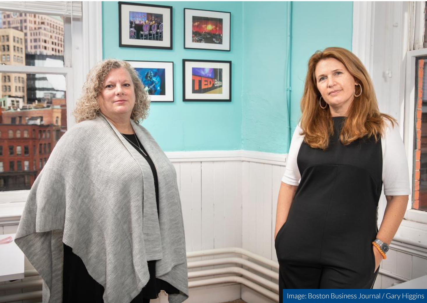 Two women are standing next to each other in a room with pictures on the wall.
