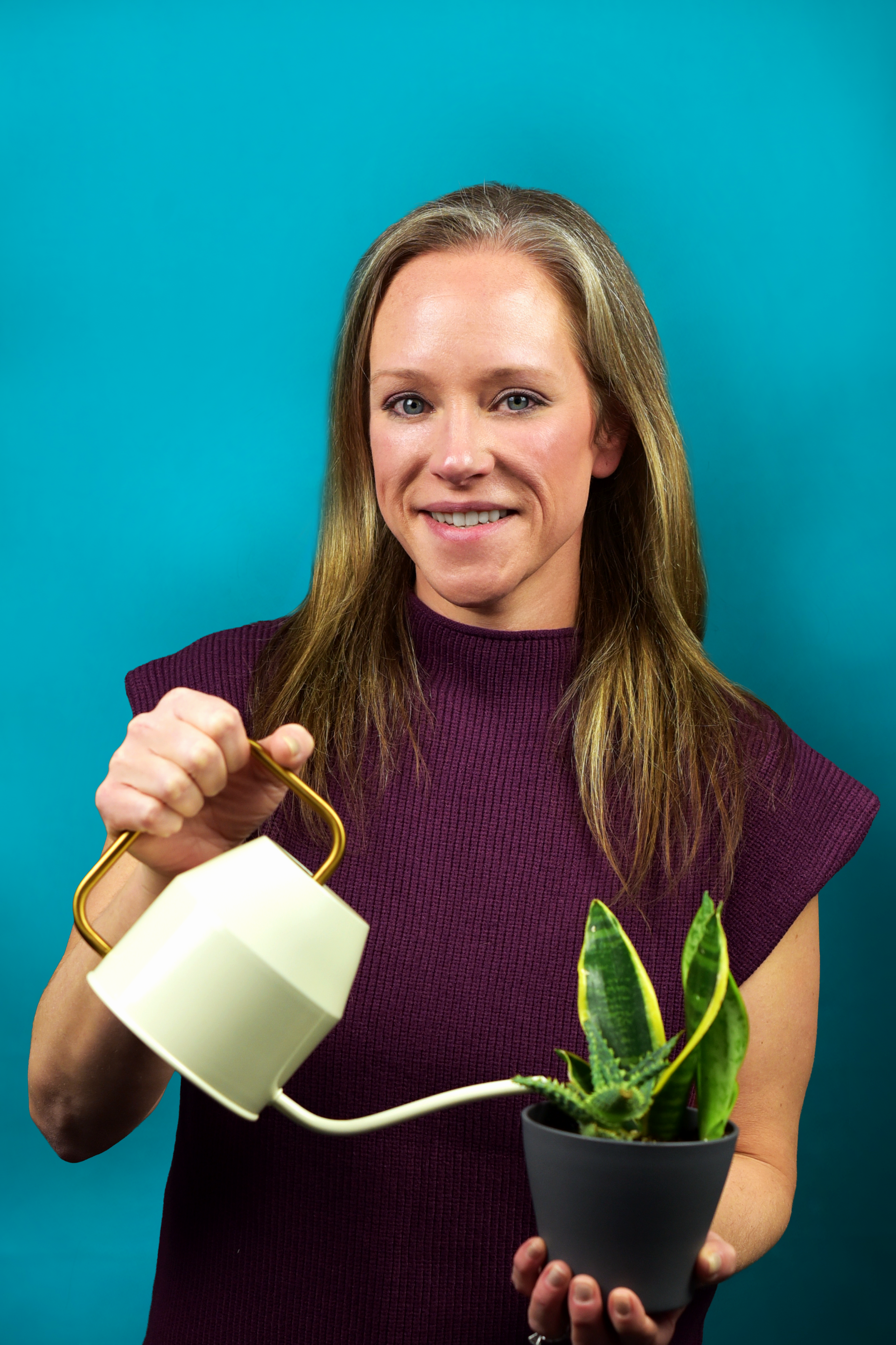 Woman watering a potted plant with a cream-colored watering can; teal background.