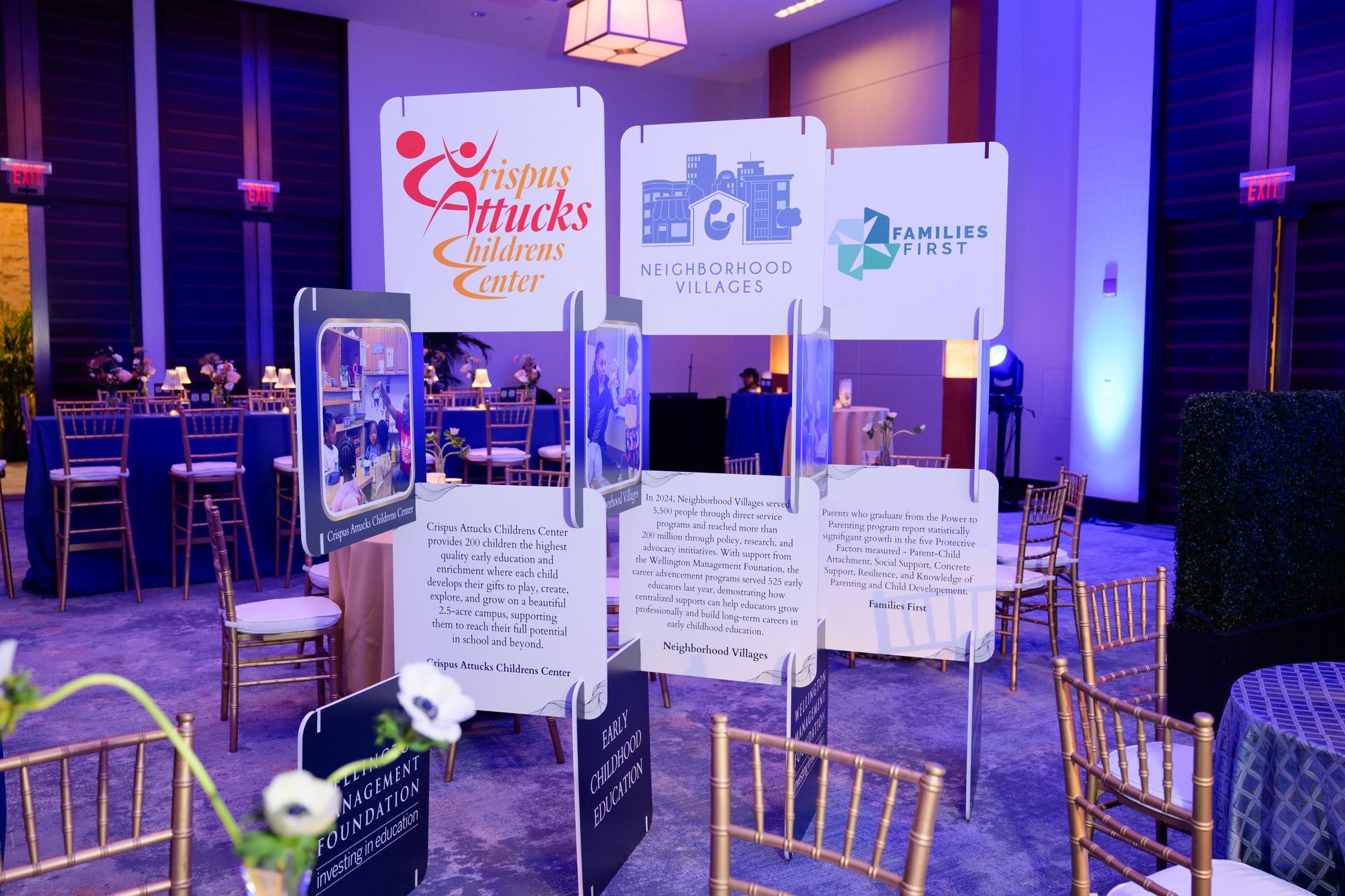 Event with informational displays; signage with logos and text, tables with chairs, and blue and gold decor.