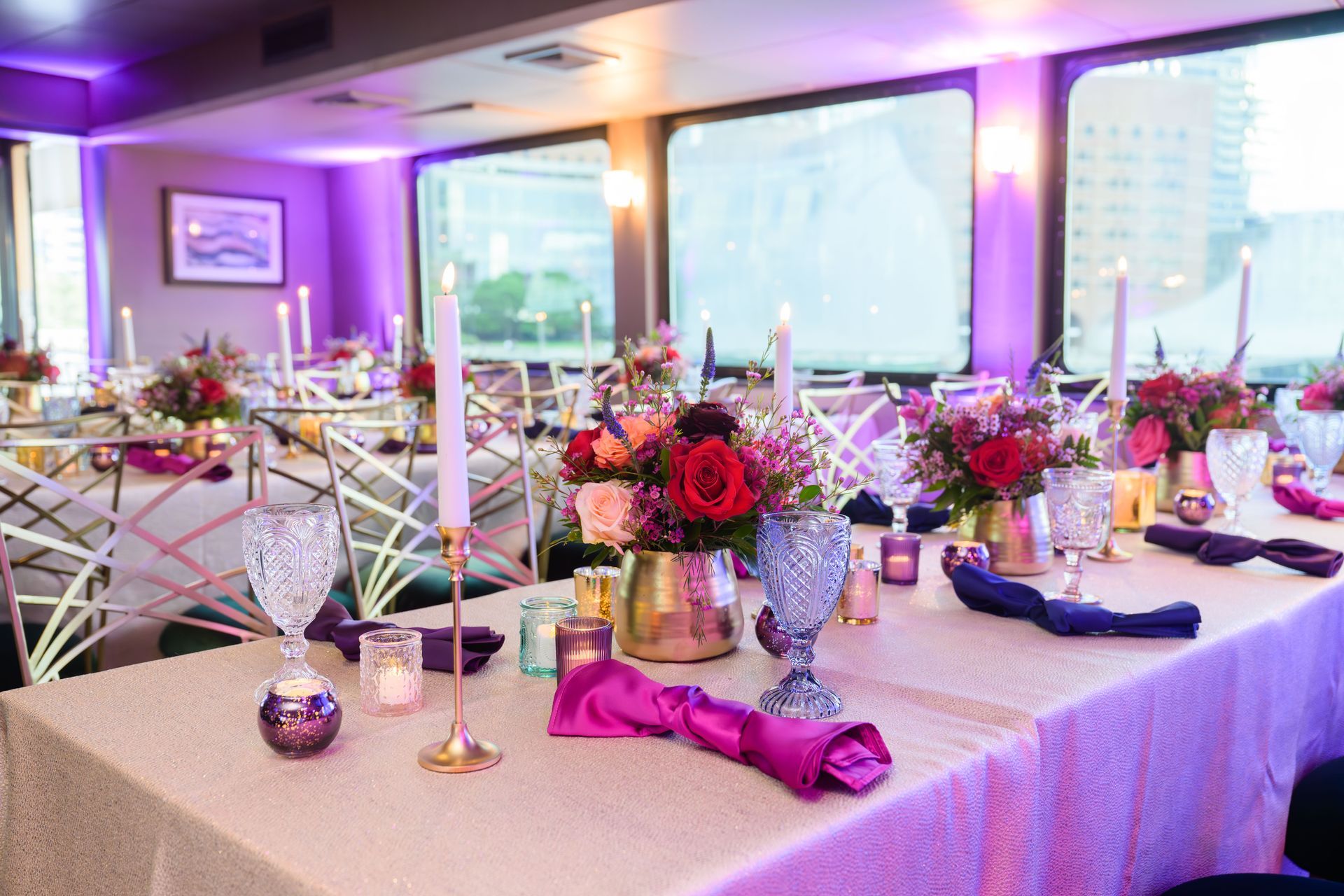 Formal dining table set with flowers, candles, and purple lighting.