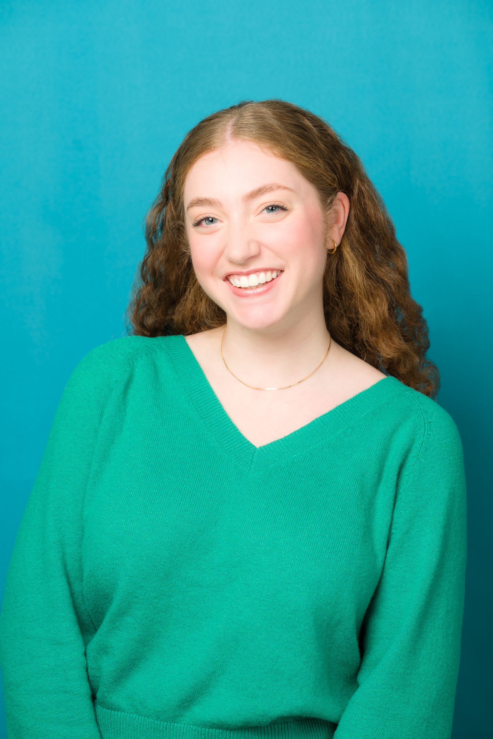 A young woman with red hair is wearing a green sweater and smiling.