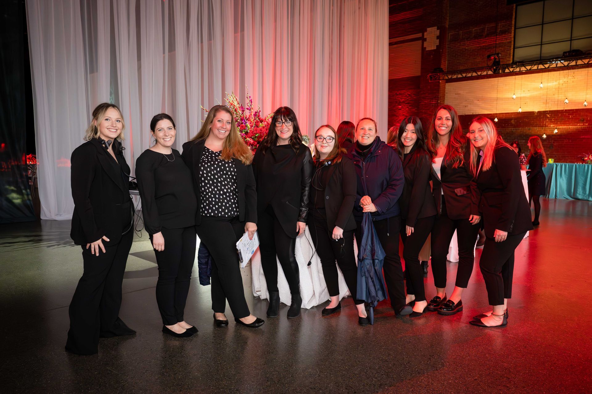 Group of people posing for a photo at a formal event, featuring a red-lit background.