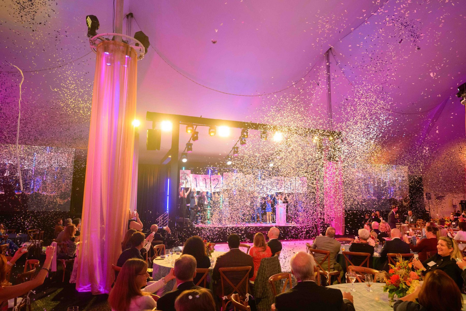A group of people are sitting at tables in a room with confetti falling from the ceiling.