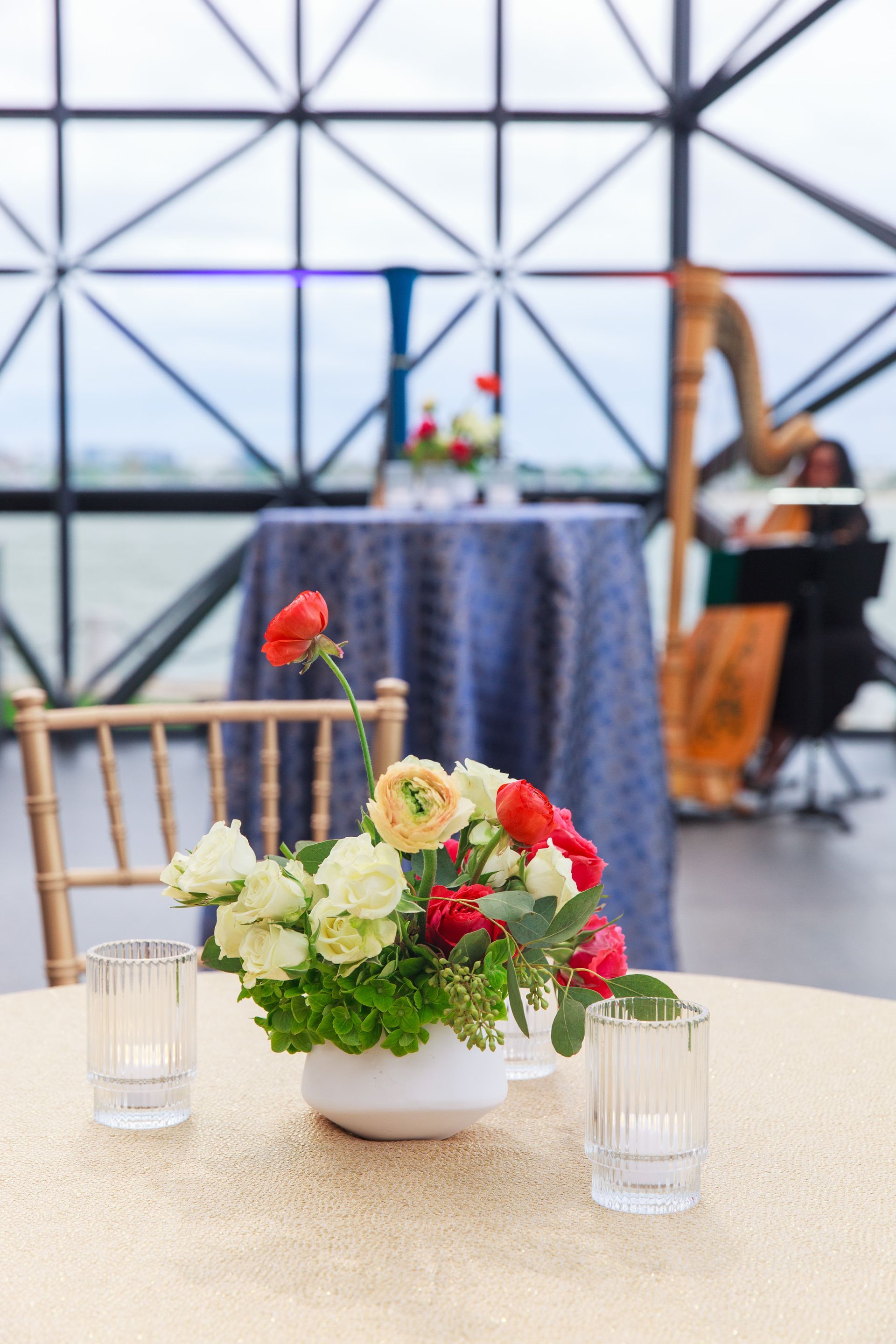 Floral centerpiece on table with a gold tablecloth, harpist in the background.