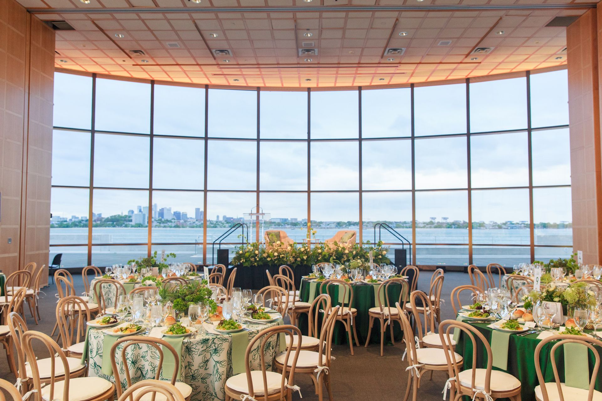 Wedding reception with round tables, green tablecloths, and waterfront view through large windows.
