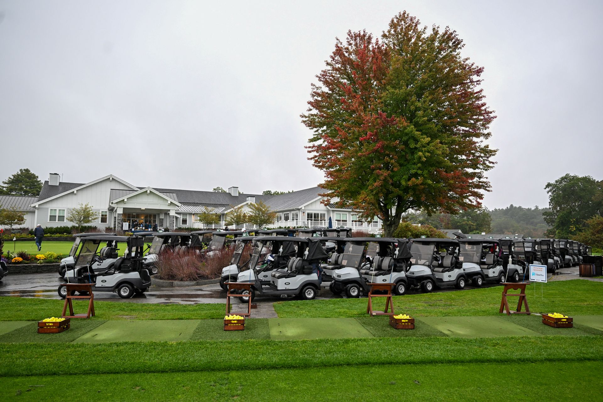 Golf carts parked on a green, facing a clubhouse, with autumn foliage in the background.