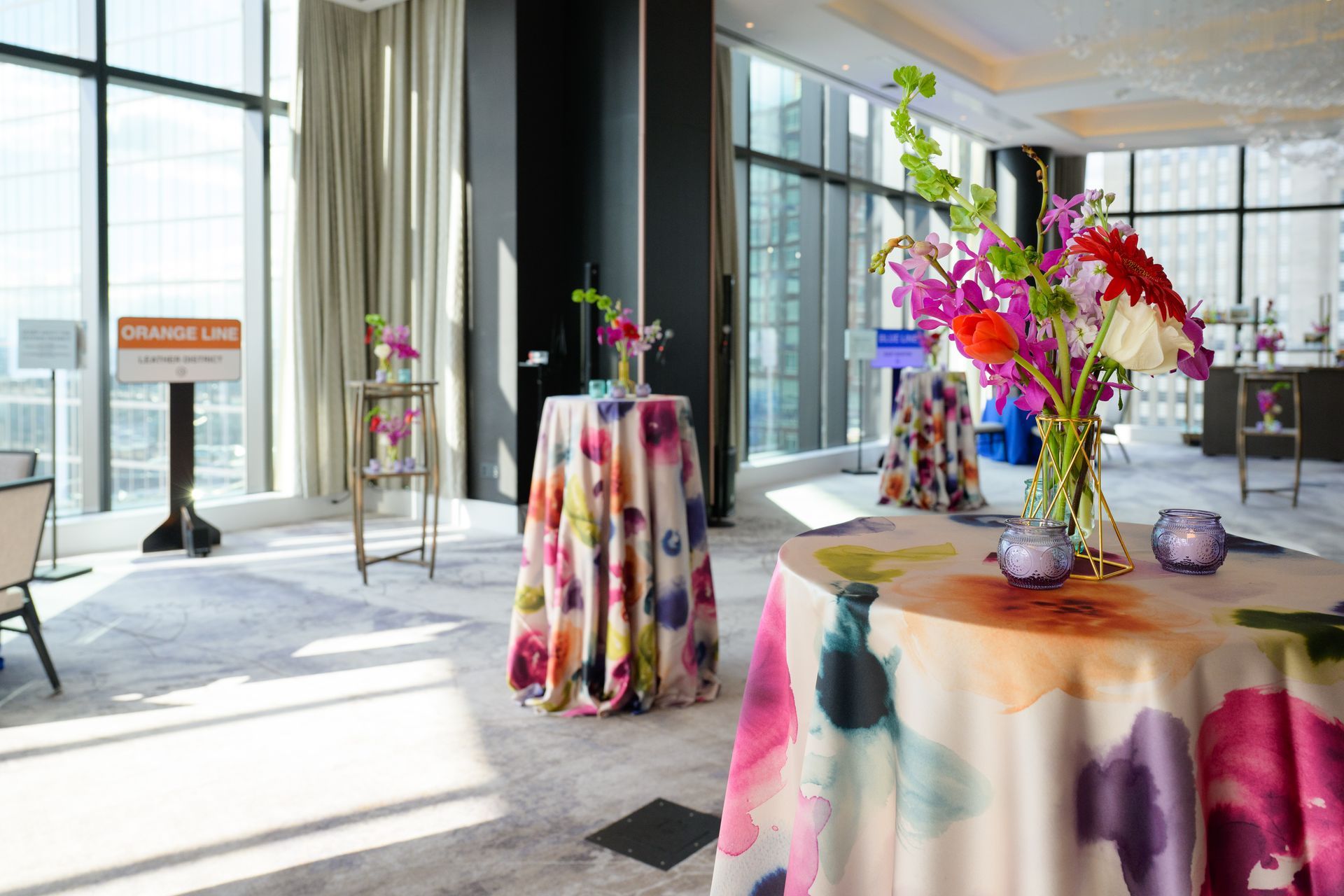 A room with floral tablecloths, vibrant flower arrangements, and large windows.
