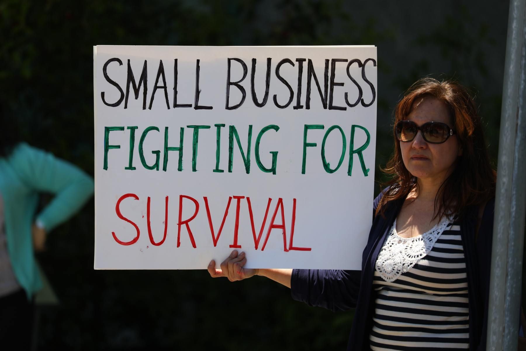 A woman is holding a sign that says small business fighting for survival
