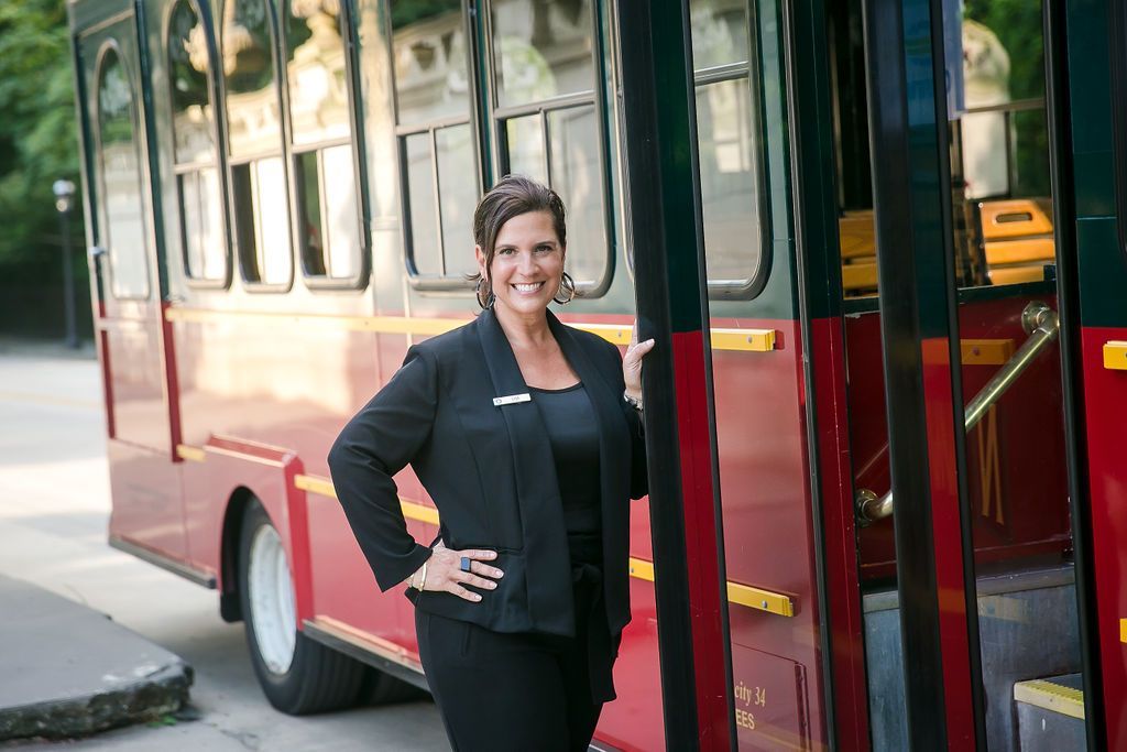 Woman in black suit stands beside a red trolley, smiling with hand on hip.