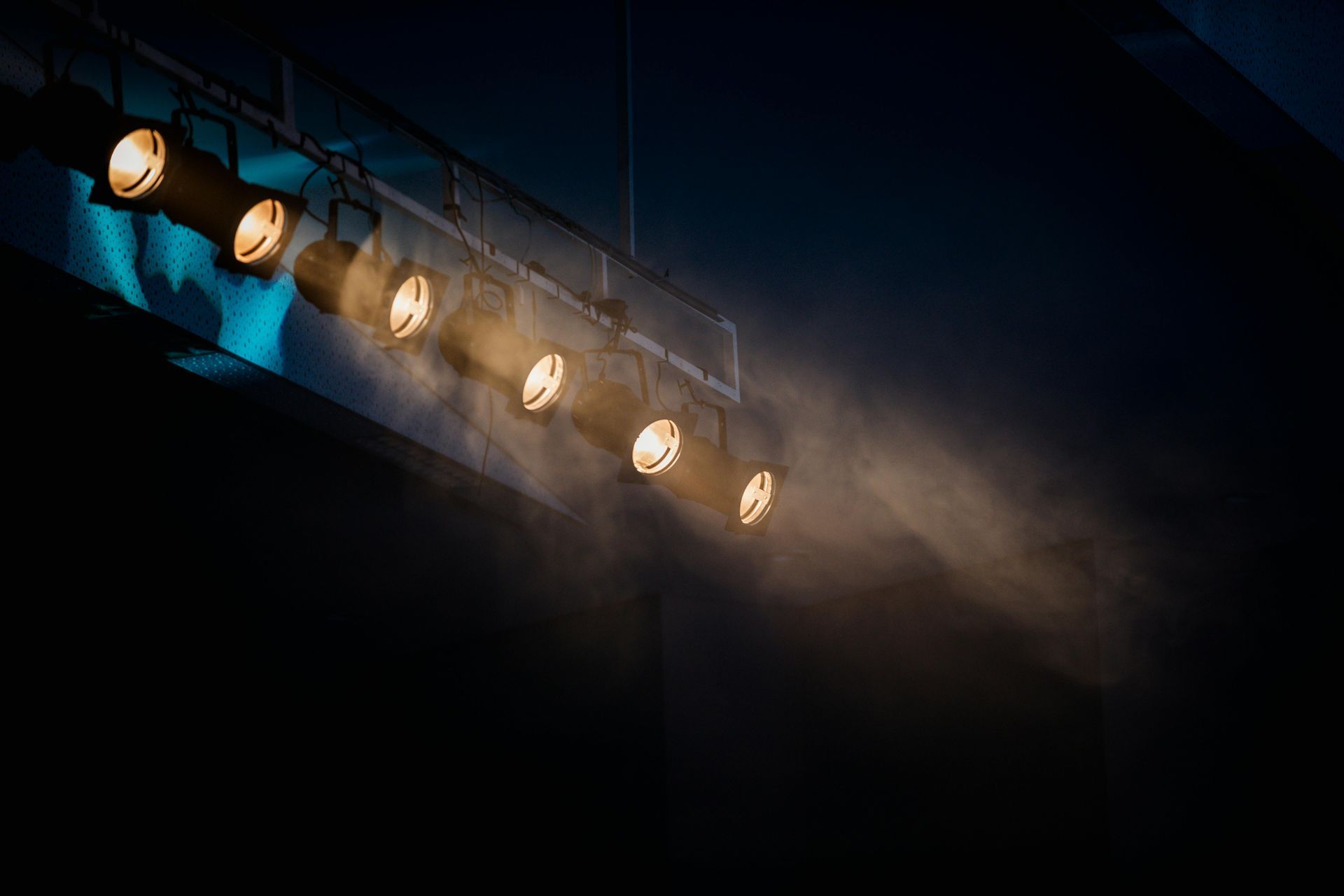 Row of stage spotlights emitting beams of light through fog.