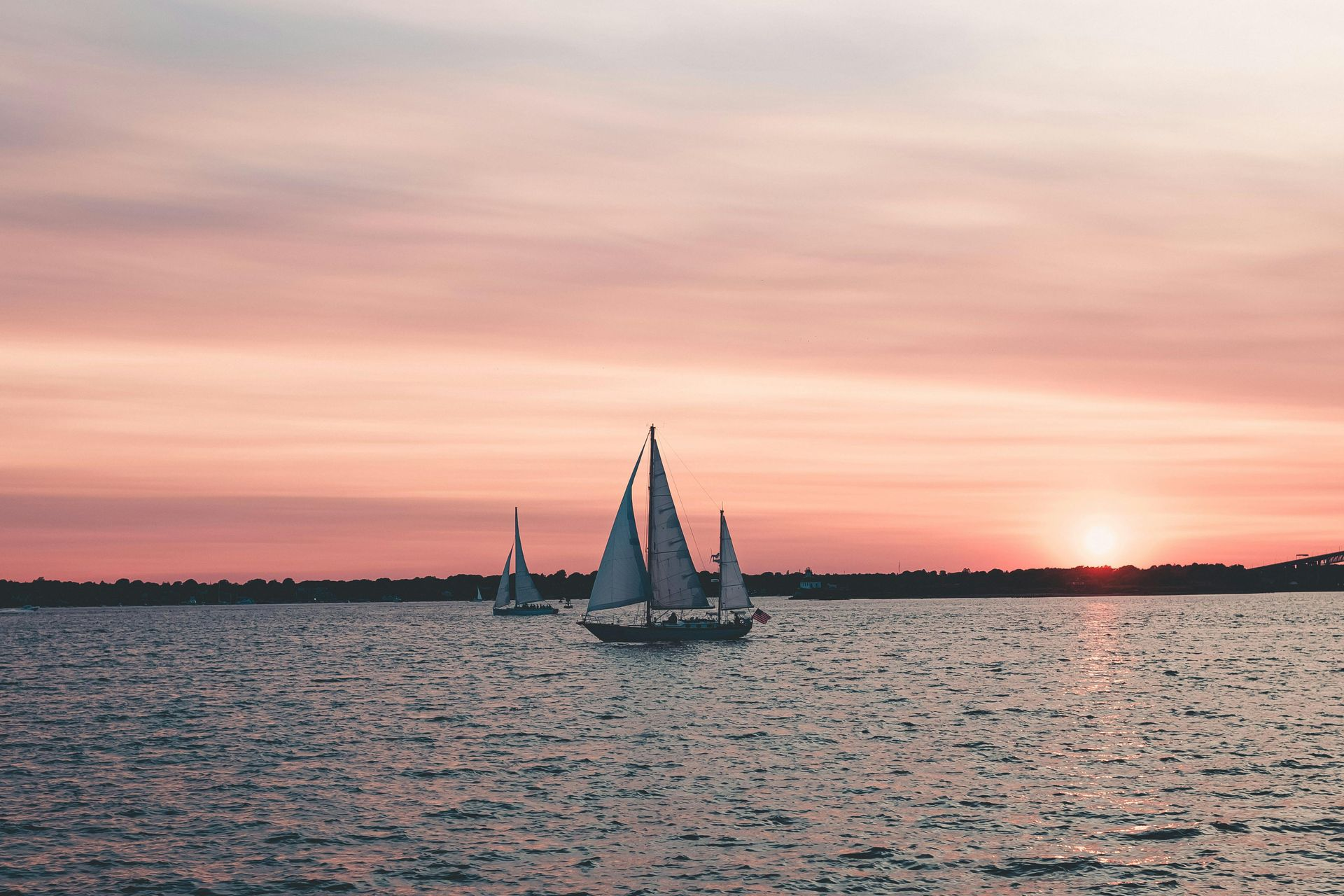 Sailboats on water at sunset, pink and orange sky.
